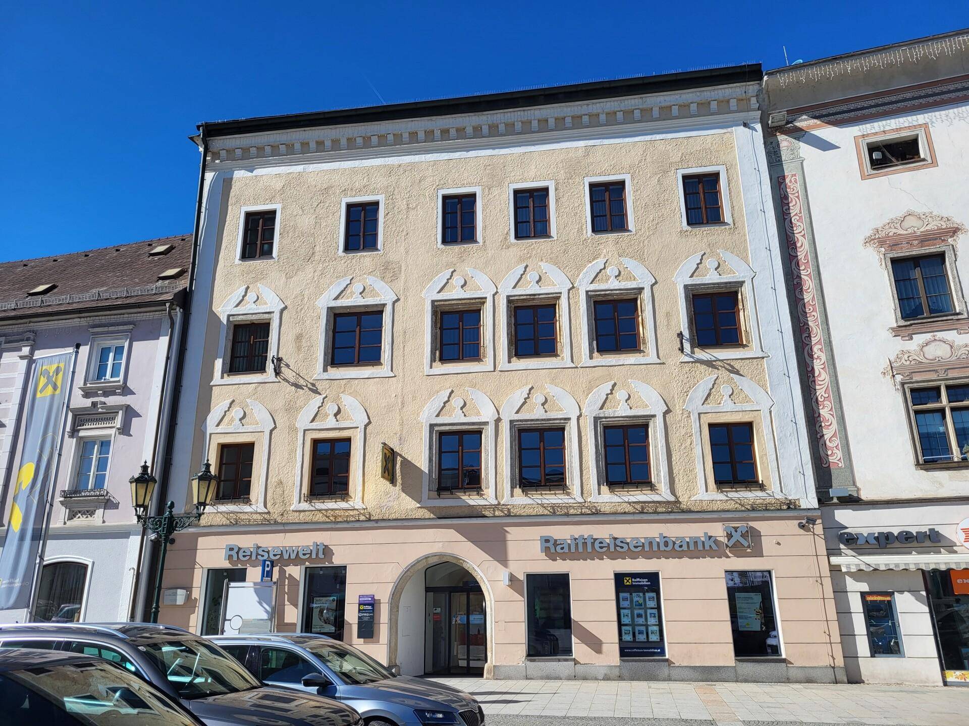 Historisches Gebäude mit einer hellen Fassade, vielen Fenstern und einer Bankfiliale im Erdgeschoss.