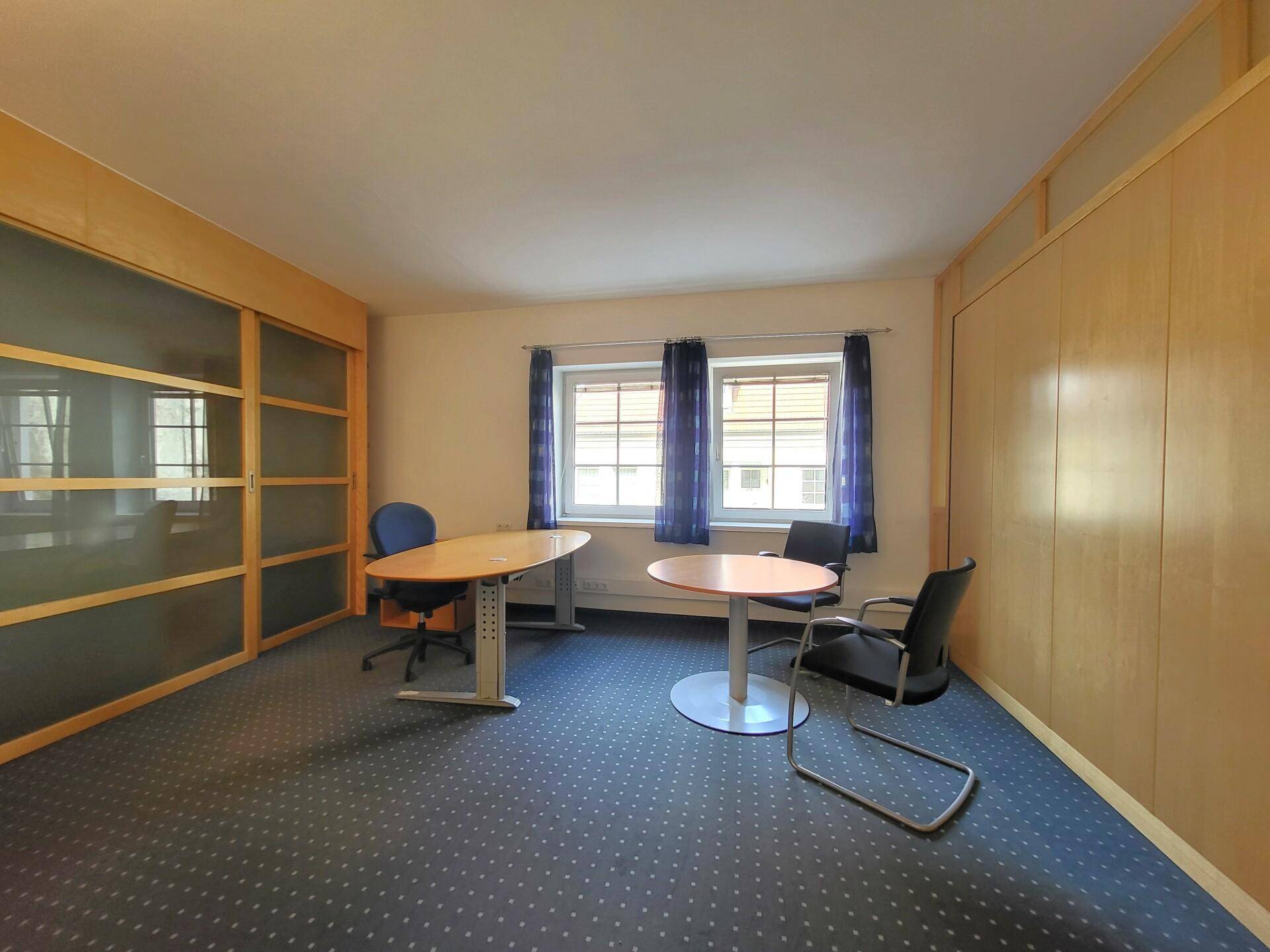 Helles Büro mit Teppichboden, Holztischen und Schiebetüren, ideal für Besprechungen oder Einzelarbeitsplätze.