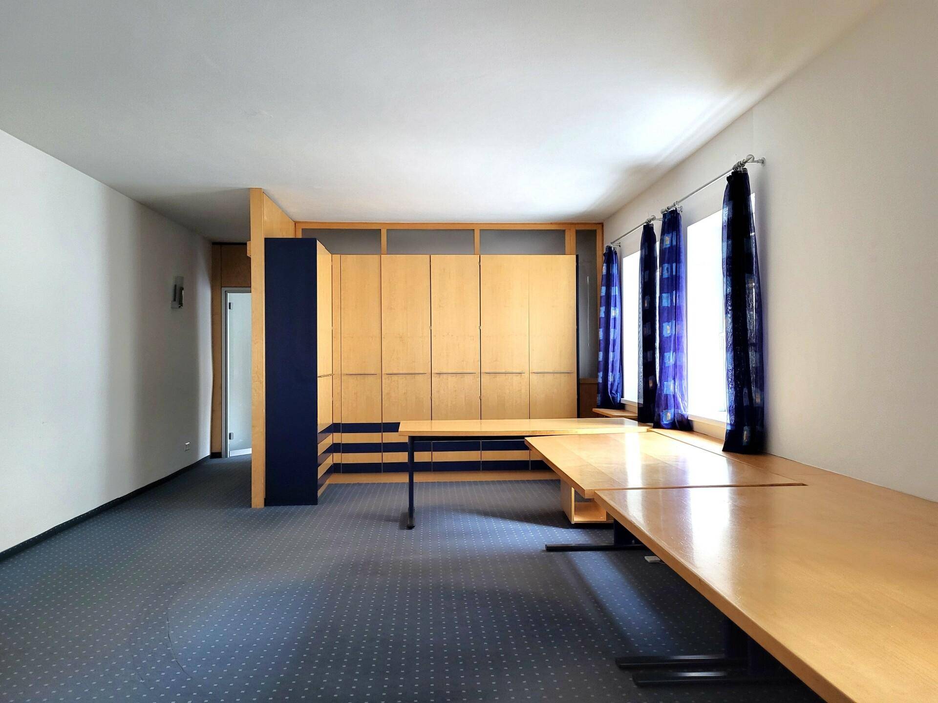 Weitläufiges Büro mit blaugrauem Teppichboden, integrierten Holzschränken und langen Arbeitstischen.