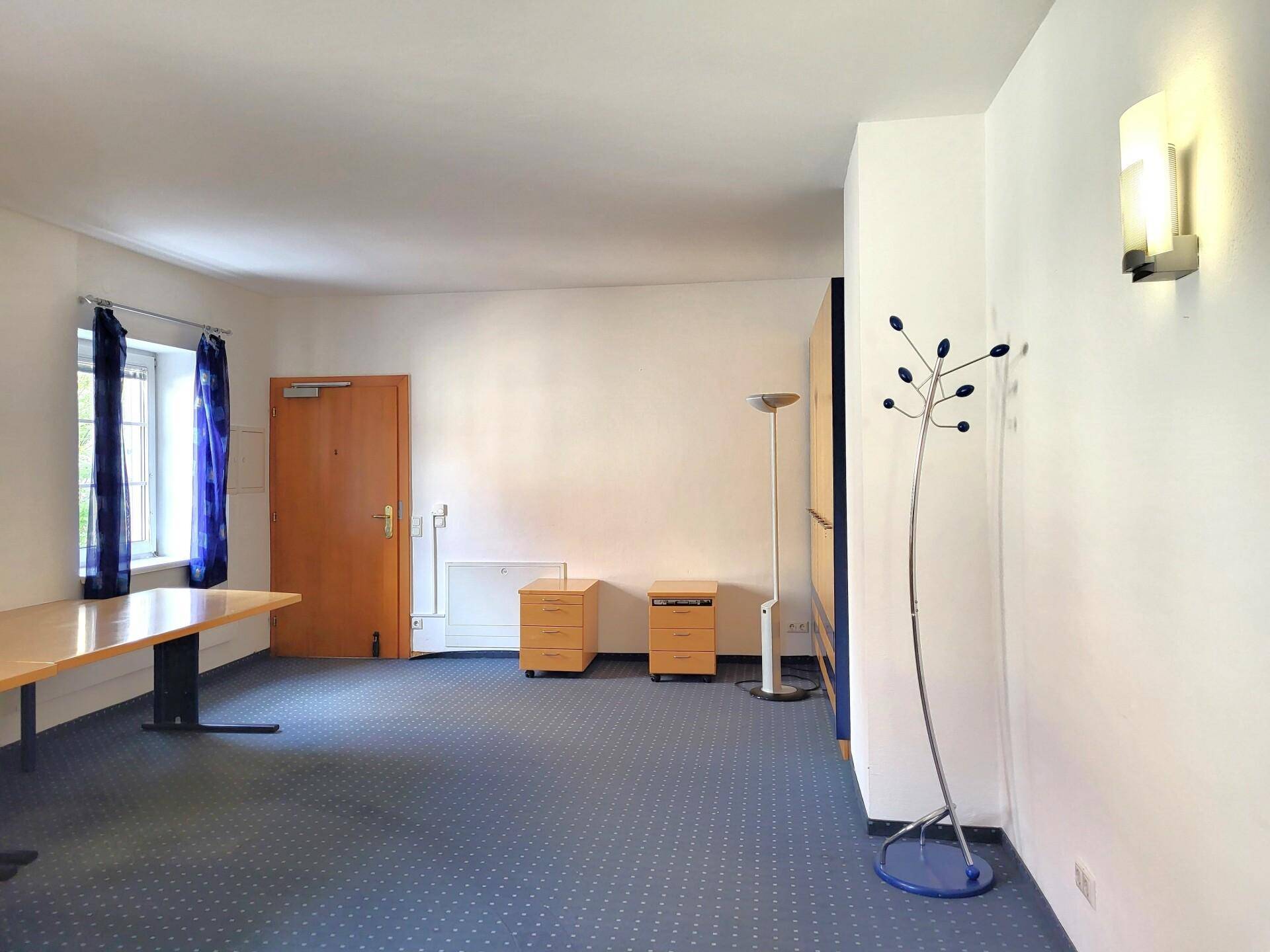 Eingangsbereich des Büros mit Teppichboden, Garderobe und einer Holztür, die zu weiteren Räumen führt.