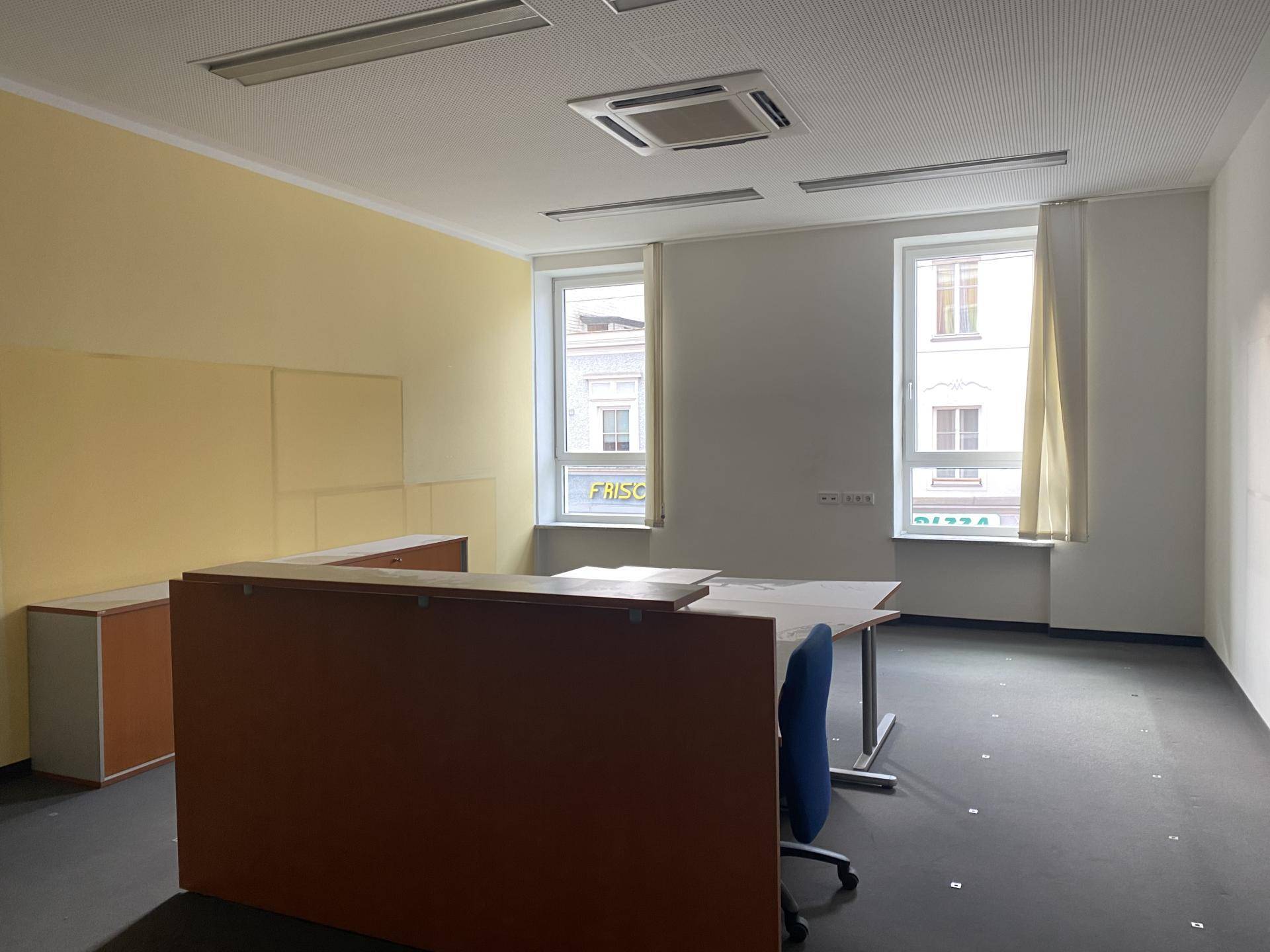 Bürofläche mit Schreibtisch und Bürostuhl, umgeben von hellen Wänden und Fenstern mit Stadtblick.