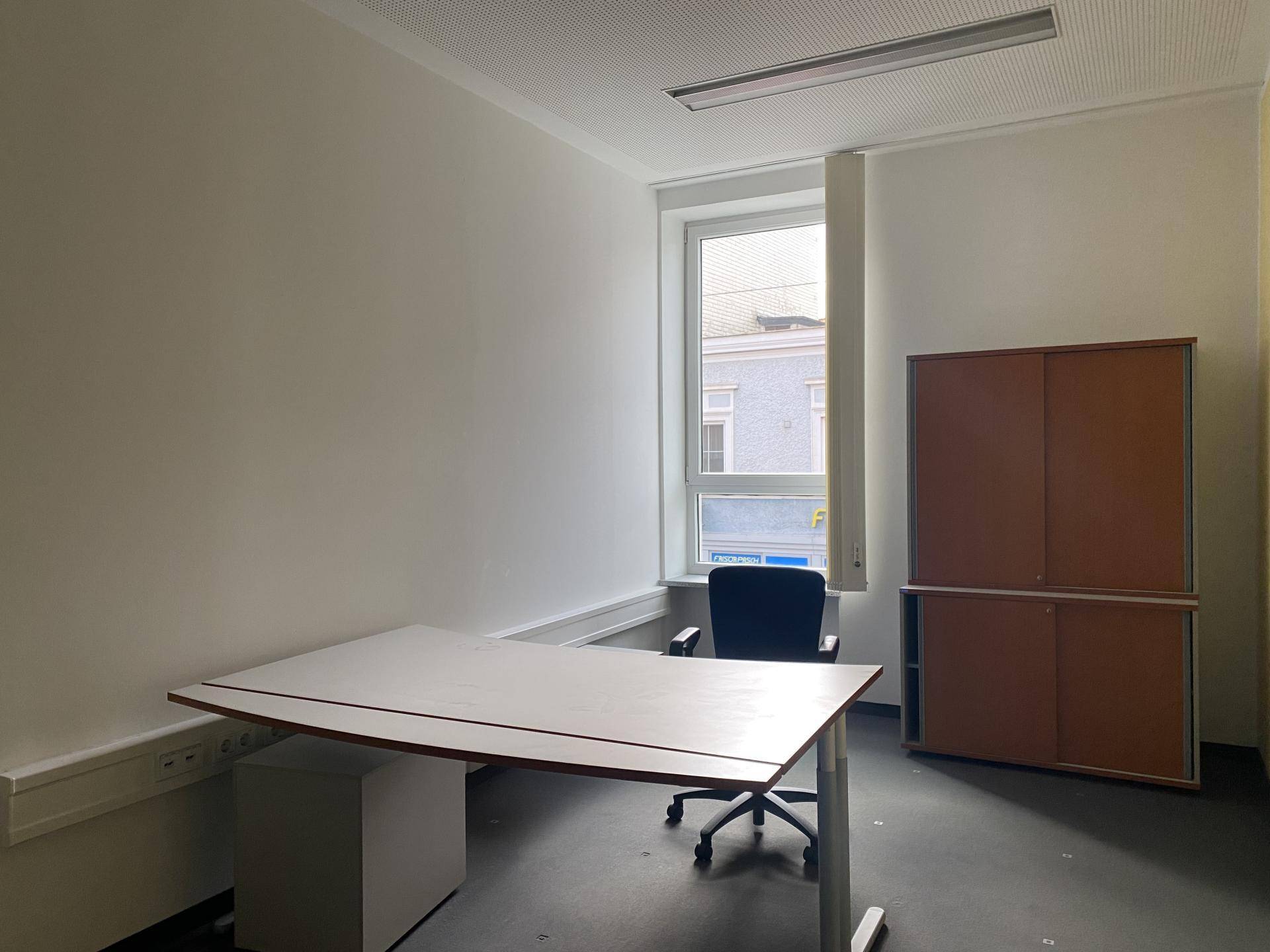 Einzelbüro mit Schreibtisch, Bürostuhl und einem großen Fenster, das viel natürliches Licht hereinlässt.