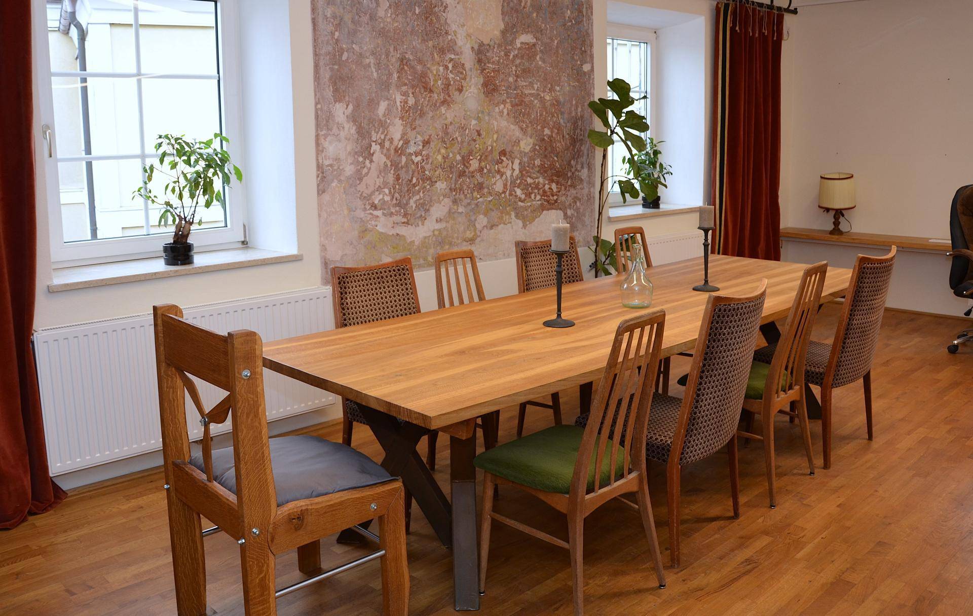 Großer Konferenztisch aus Holz mit verschiedenen Stühlen in einem Raum mit rustikaler Wand und großen Fenstern.