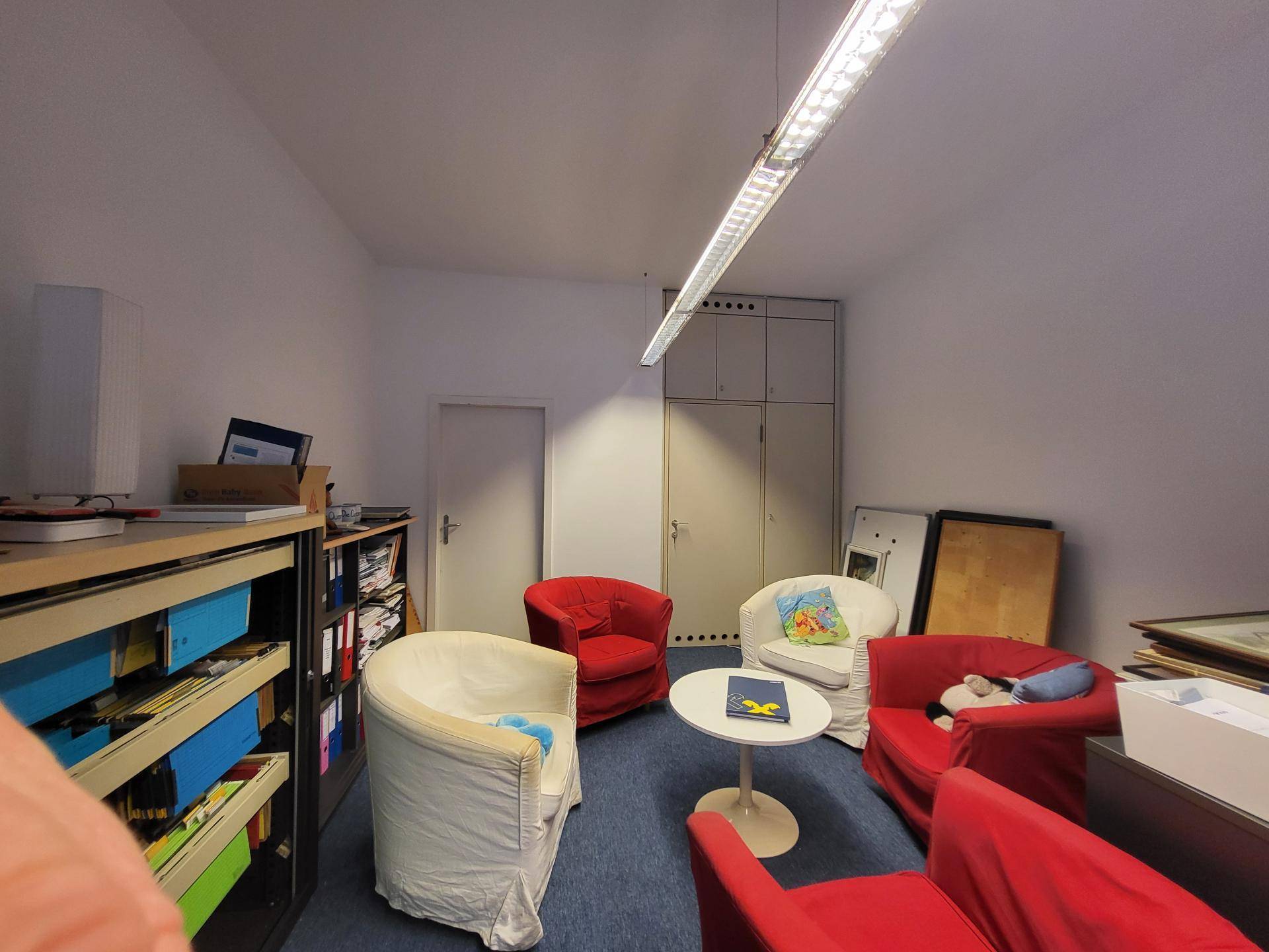 Gemütlicher Bürobereich mit roten und weißen Sesseln, einem kleinen Tisch und integrierten Aktenschränken.