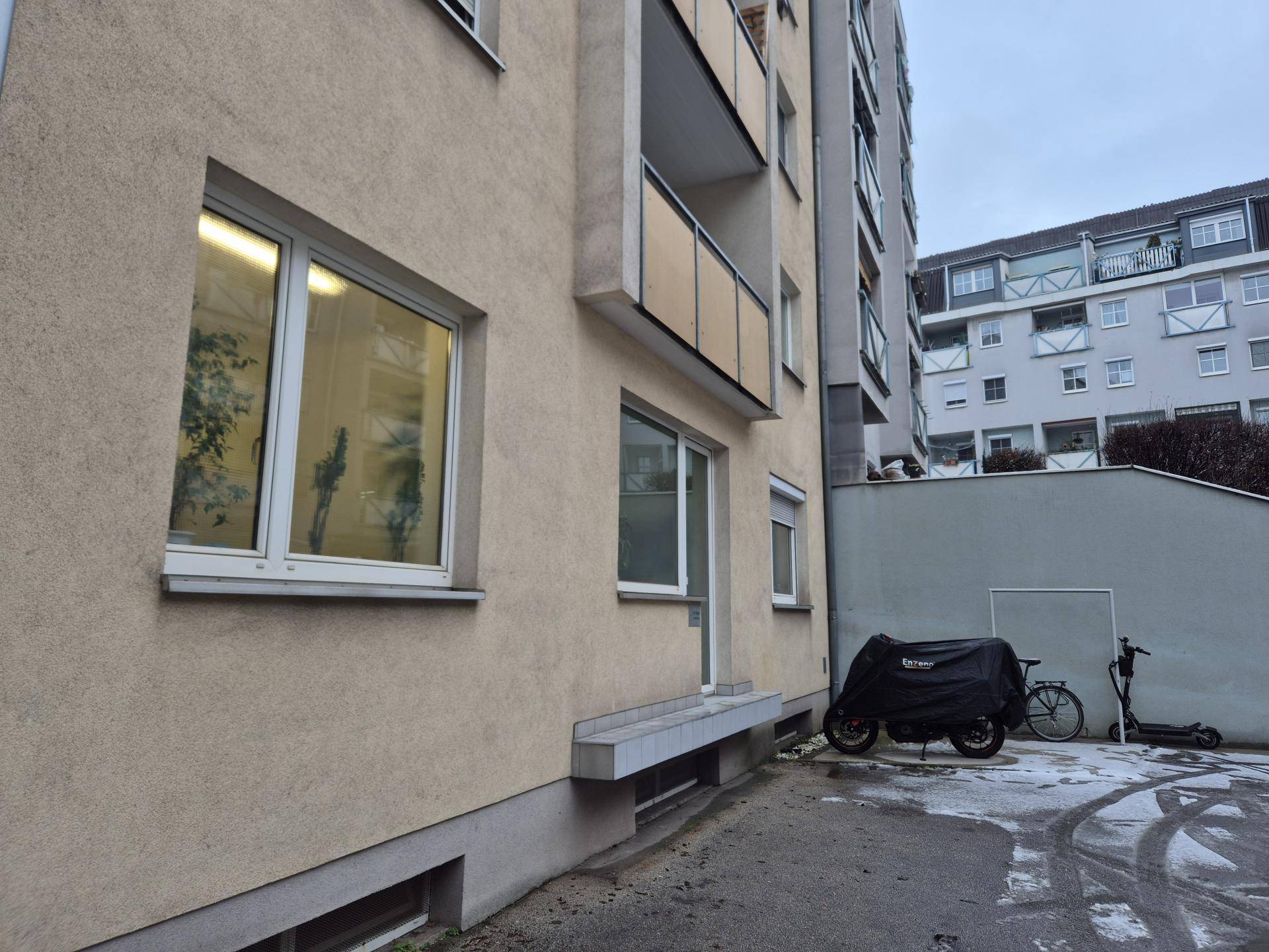 Seitenansicht eines Wohngebäudes mit Balkonen und einem überdachten Motorrad im Vordergrund auf dem Hof.