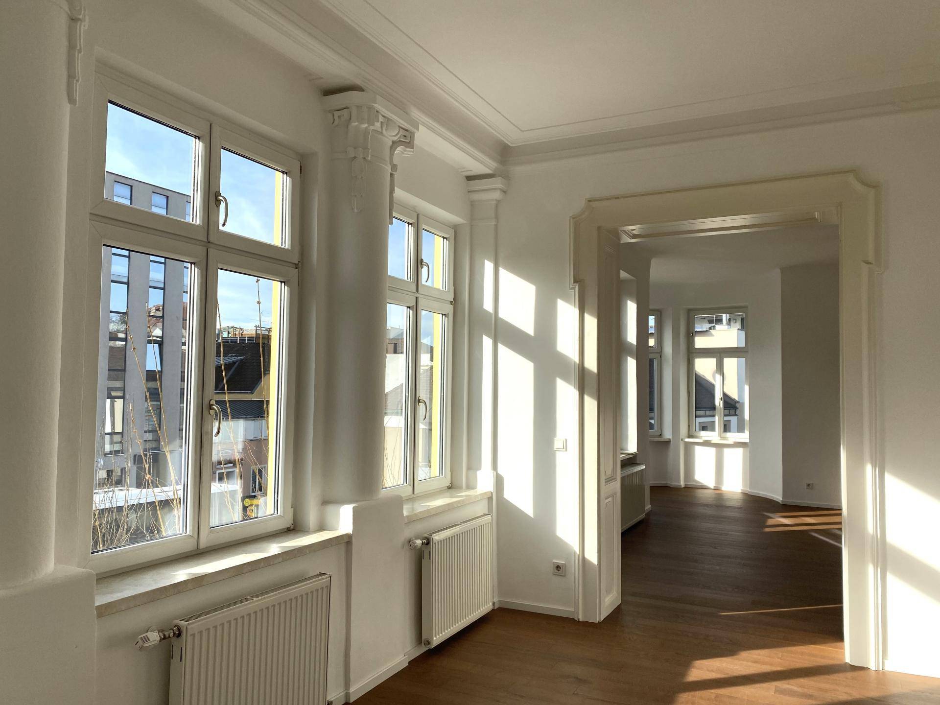 Lichtdurchfluteter Wohnbereich mit hohen Fenstern, Säulen und Blick auf die Stadt.