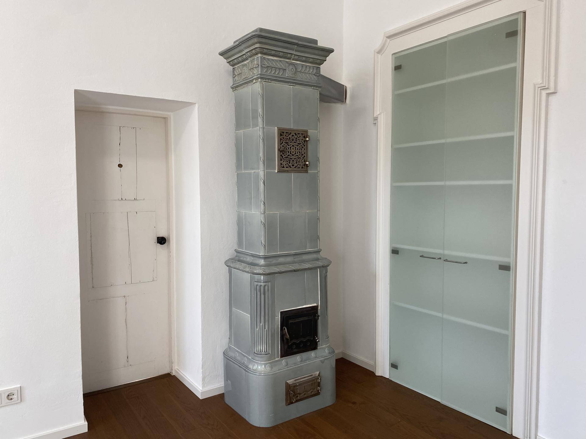 Raum mit traditionellem Kachelofen, Holzboden und moderner Glastür.