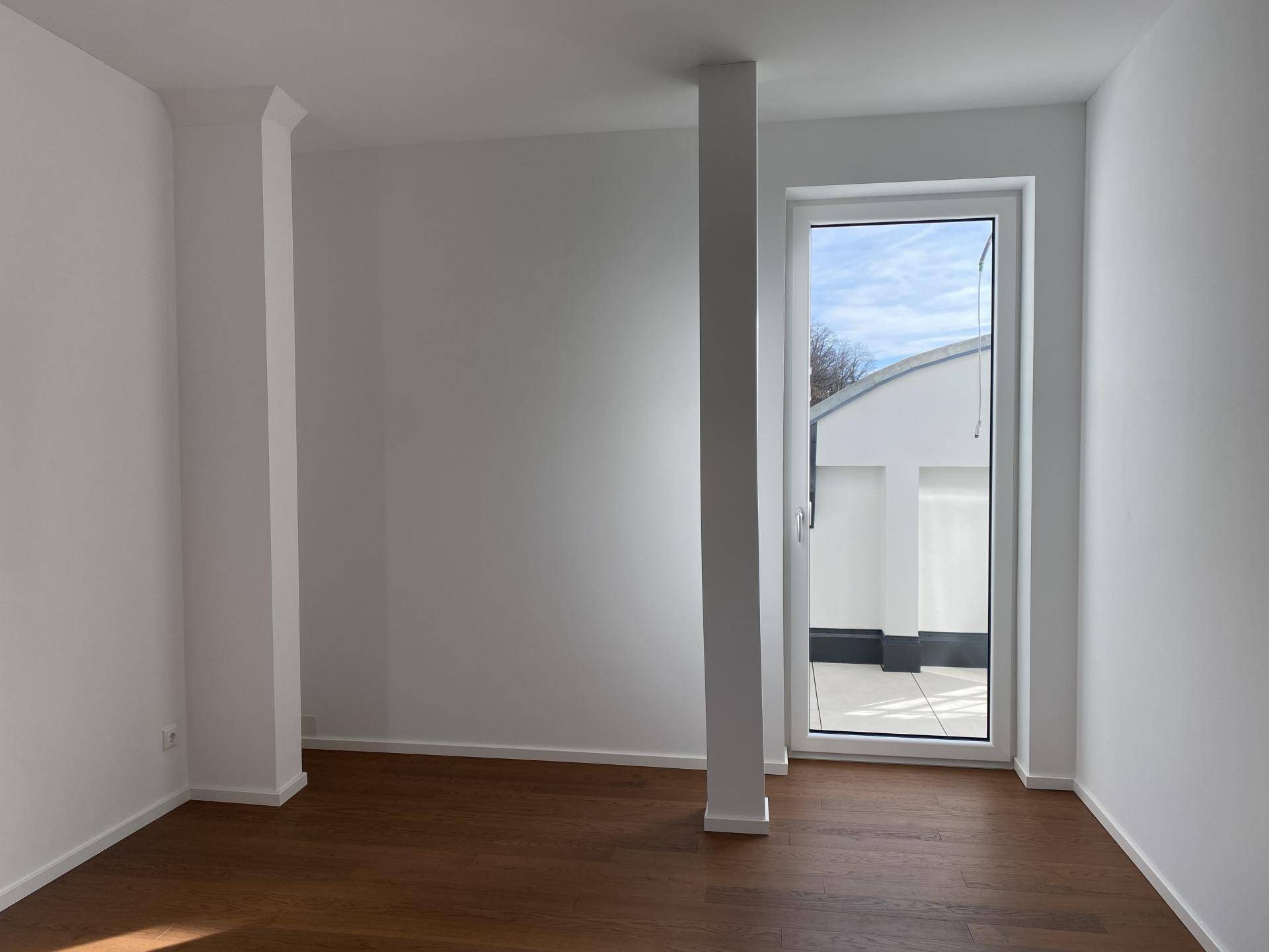 Heller Raum mit Holzboden und Zugang zu einem Außenbereich, ideal für flexible Nutzung.
