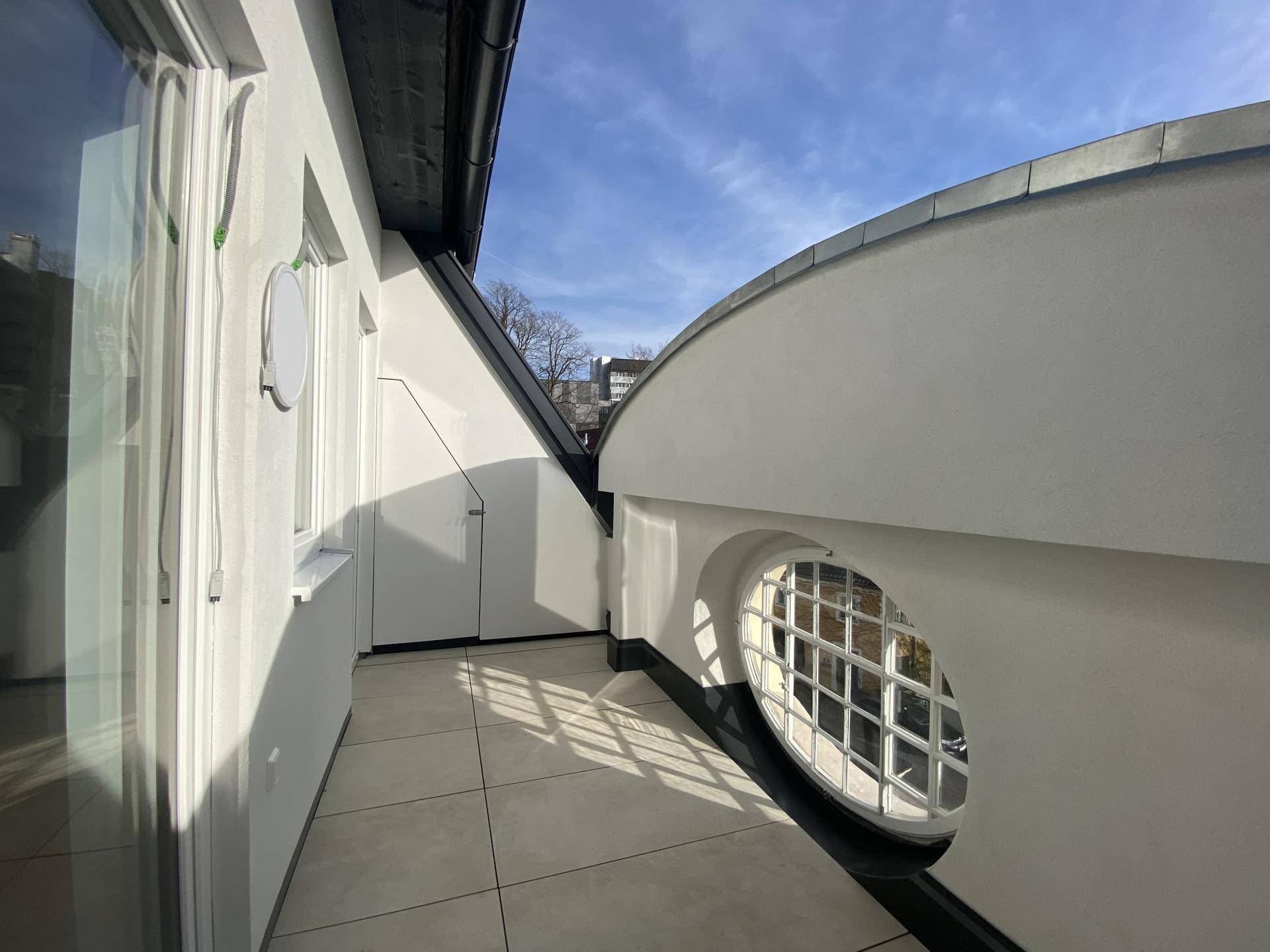 Sonniger Terrassenbereich mit Fliesenboden und geschwungener Brüstung unter blauem Himmel.
