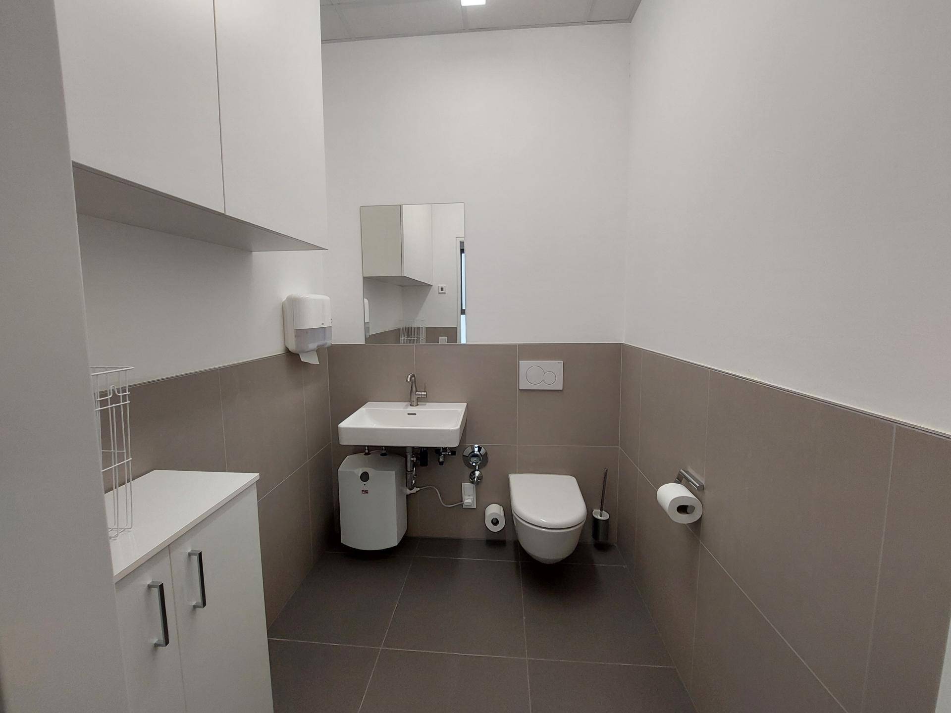 Modernes WC mit Wand-WC, Waschbecken und hellen Fliesen an Wänden und Boden, sauber und funktional.