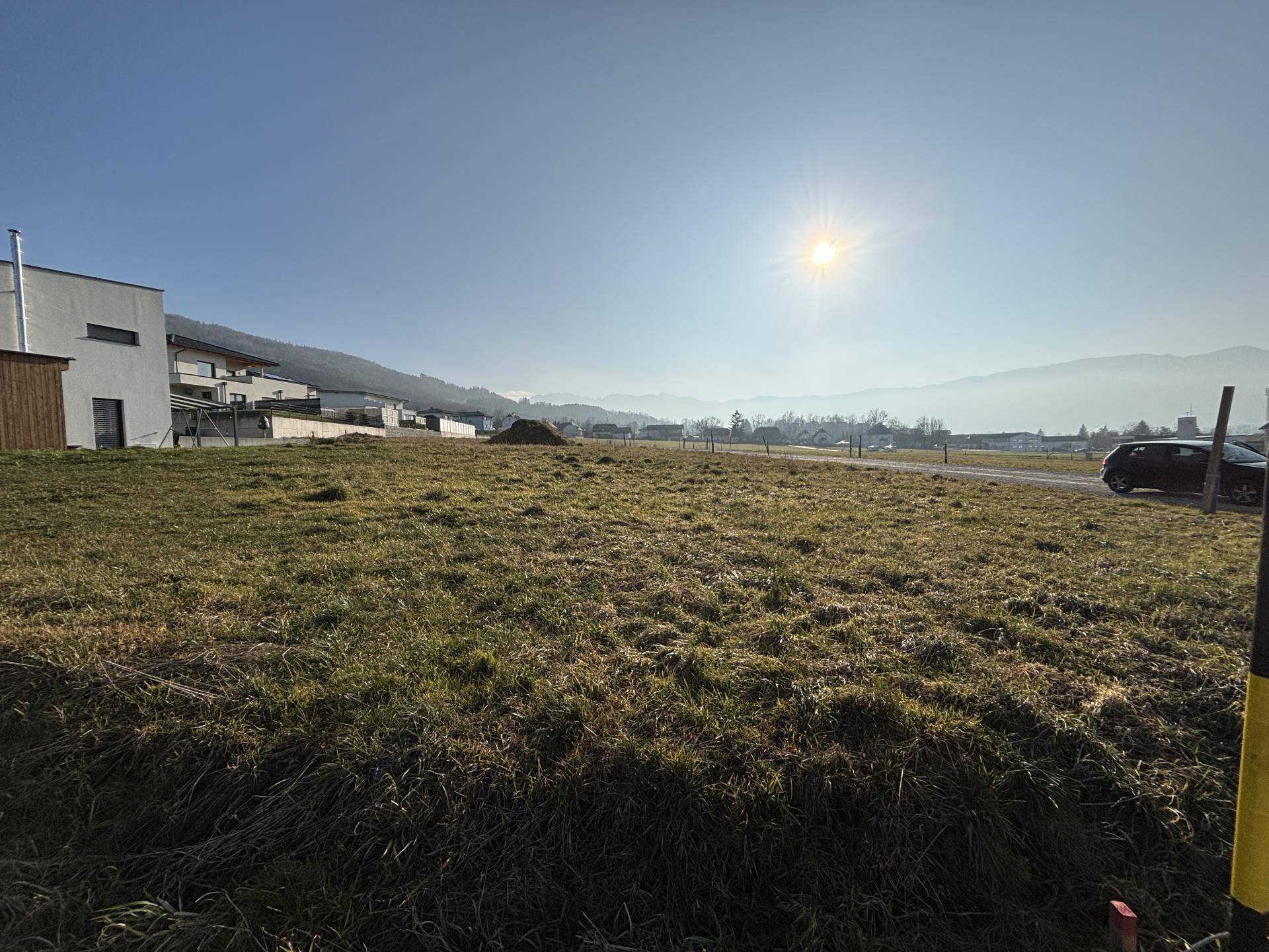 Sonniges, offenes Feld mit Blick auf moderne Architektur und die umliegende Berglandschaft.