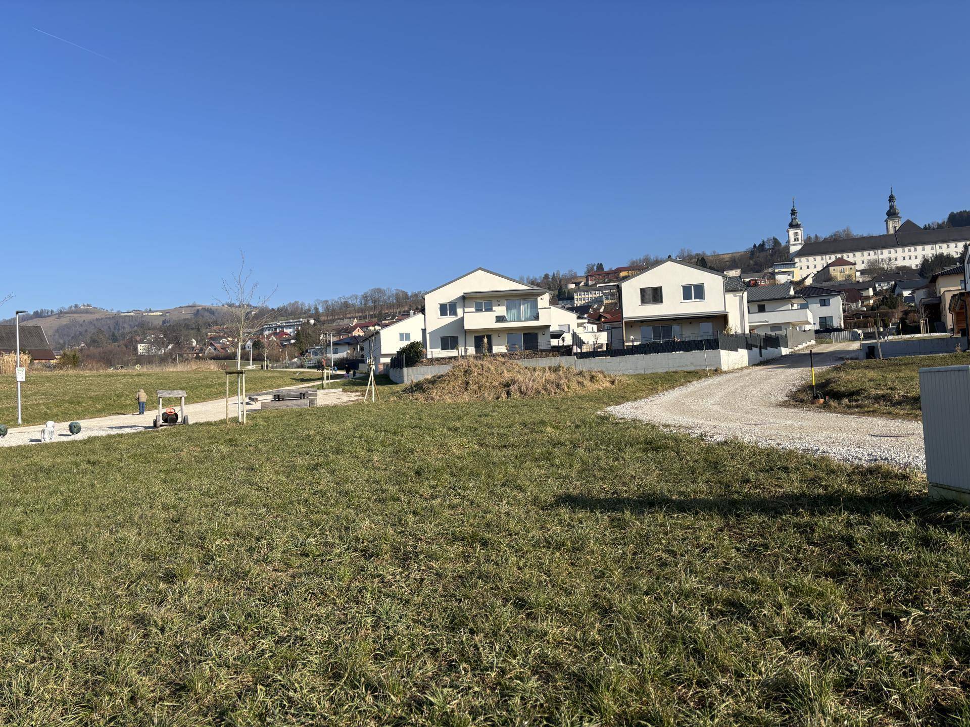 Offenes Feld mit Blick auf moderne Häuser und eine historische Kirche in der hügeligen Landschaft.