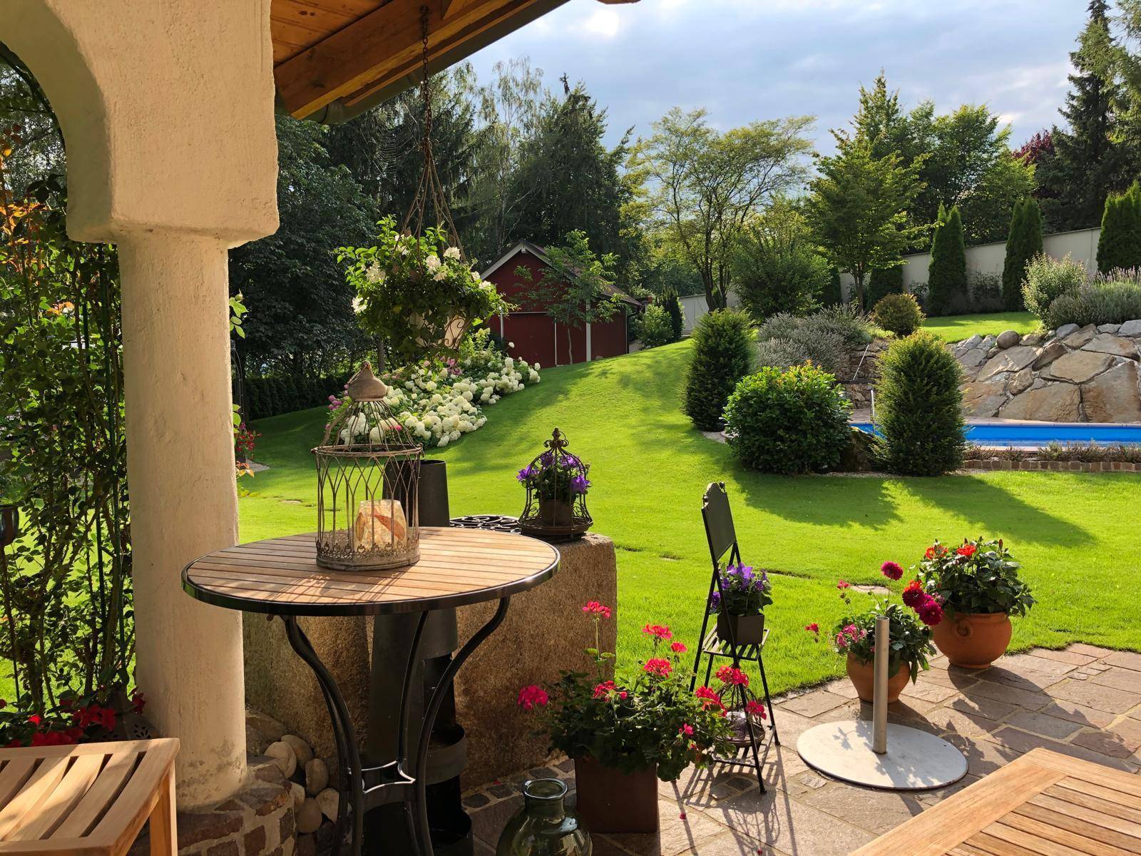 Gemütliche überdachte Terrasse mit Gartenmöbeln und Blick auf den gepflegten Garten und Poolbereich.