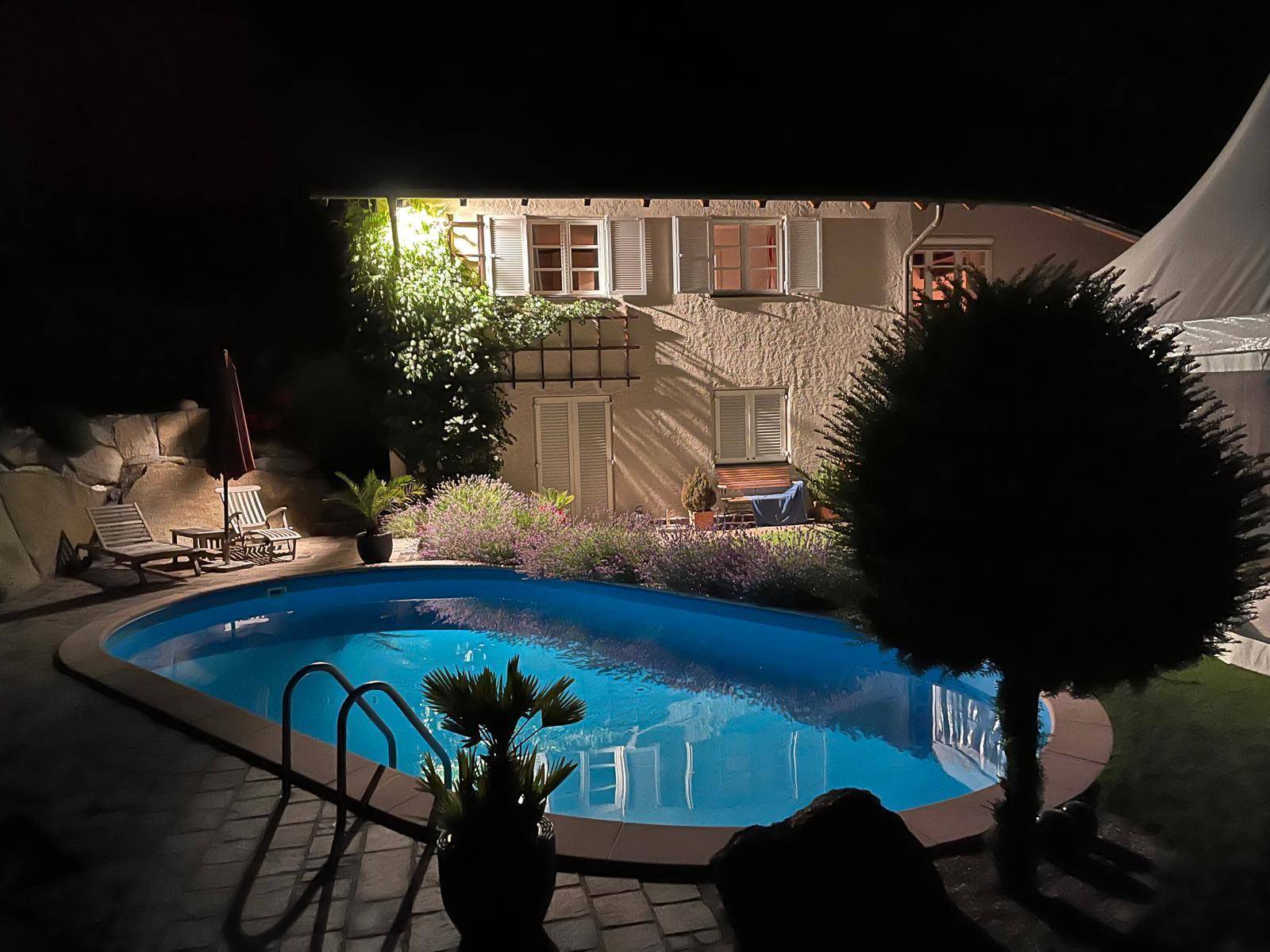 Beleuchteter Außenbereich bei Nacht mit Schwimmbecken und der Fassade des Hauses.