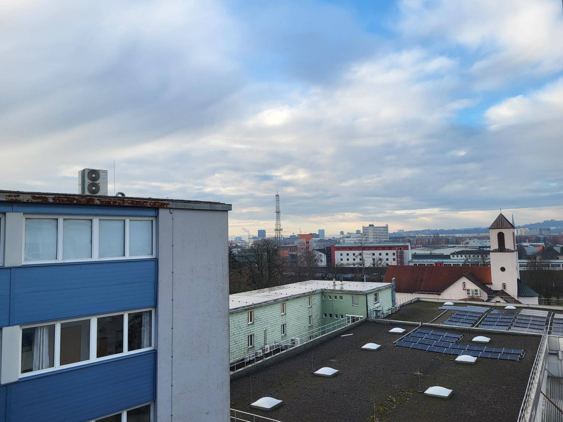 Weitblick über eine Stadtlandschaft mit verschiedenen Gebäuden und Solaranlagen auf einem Dach.