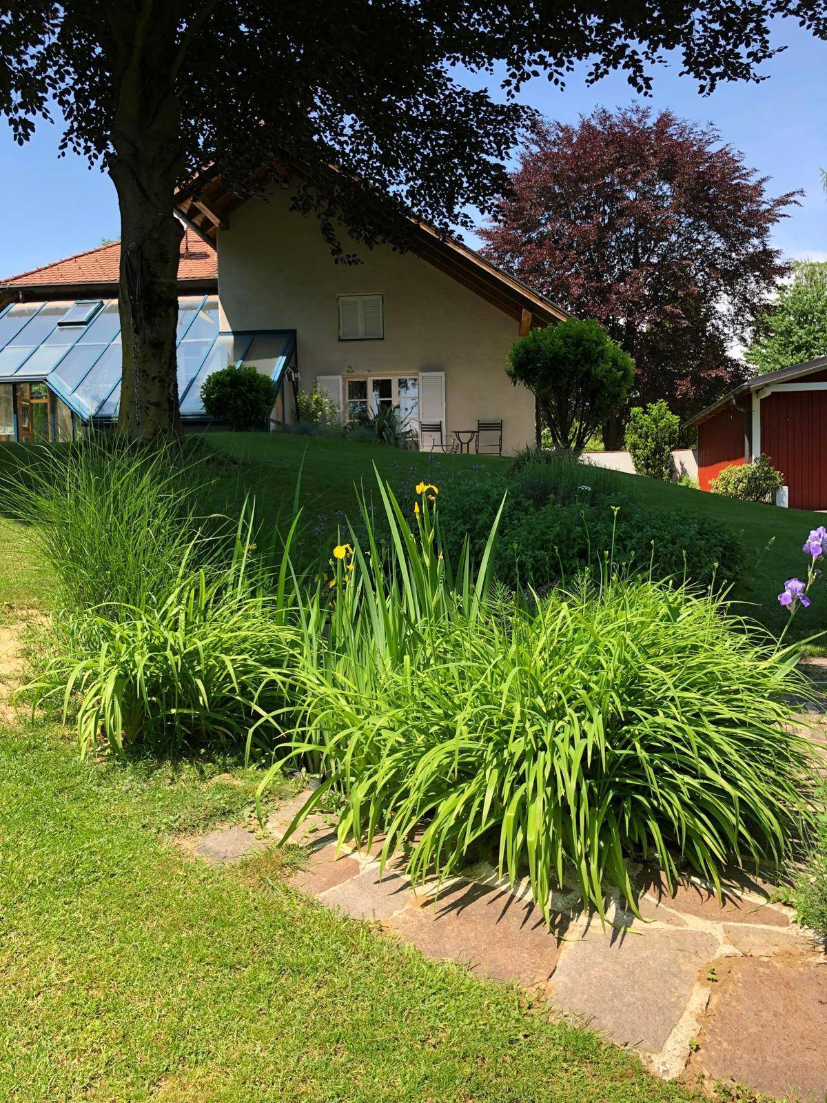 Gepflegter Garten mit üppiger Vegetation, Steinpfaden und dem Haus im Hintergrund.