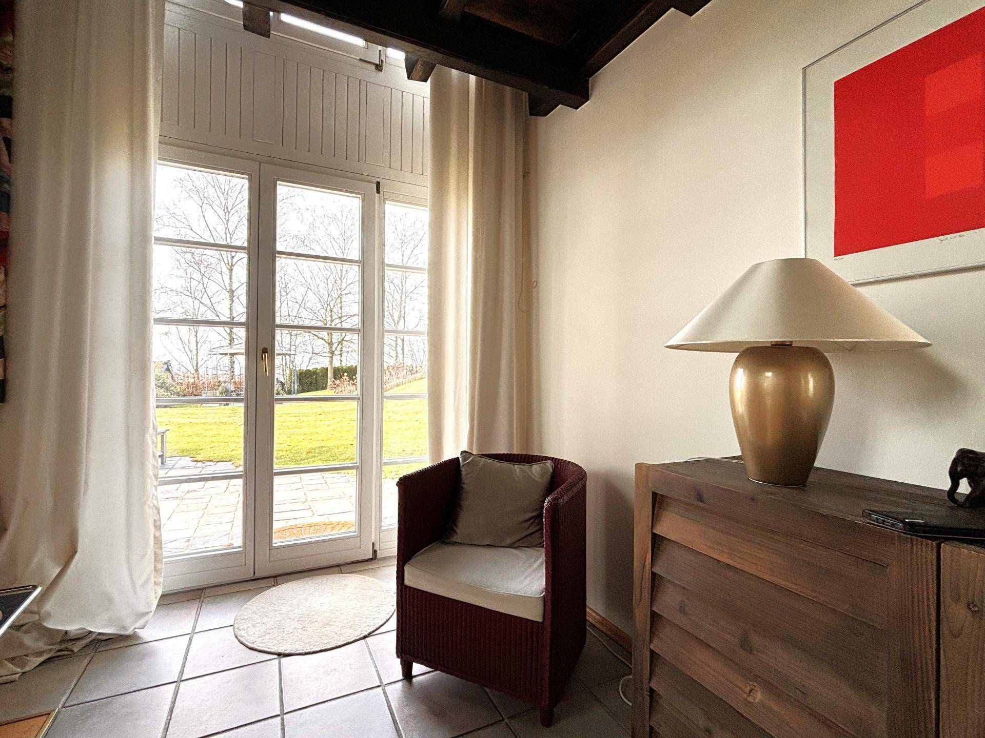 Gemütliche Ecke mit Sessel, Stehlampe und Zugang zum Garten durch große Fenstertüren.