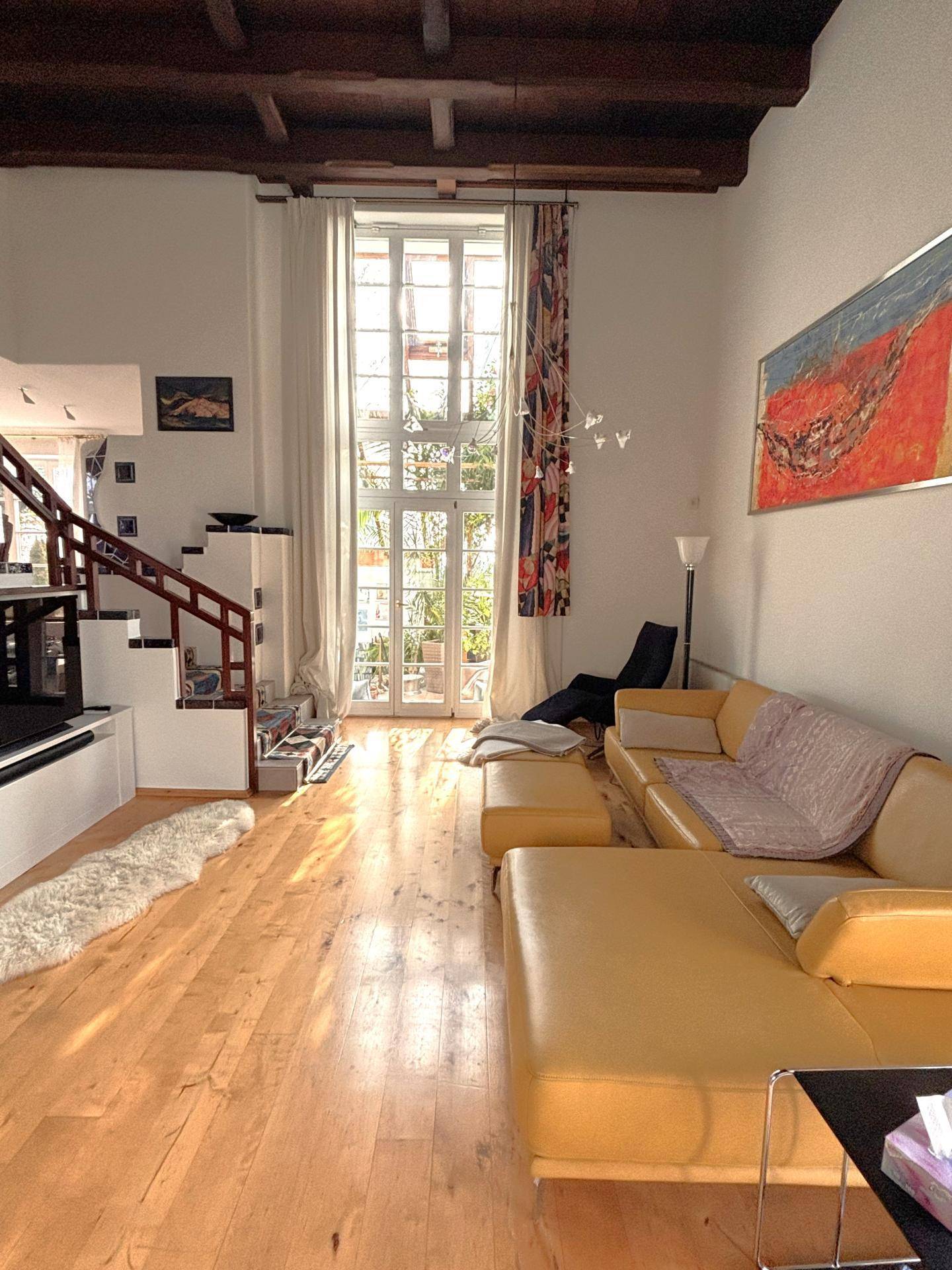 Geräumiges Wohnzimmer mit hohen Decken, Holzbalken und großem Fenster zum Garten.
