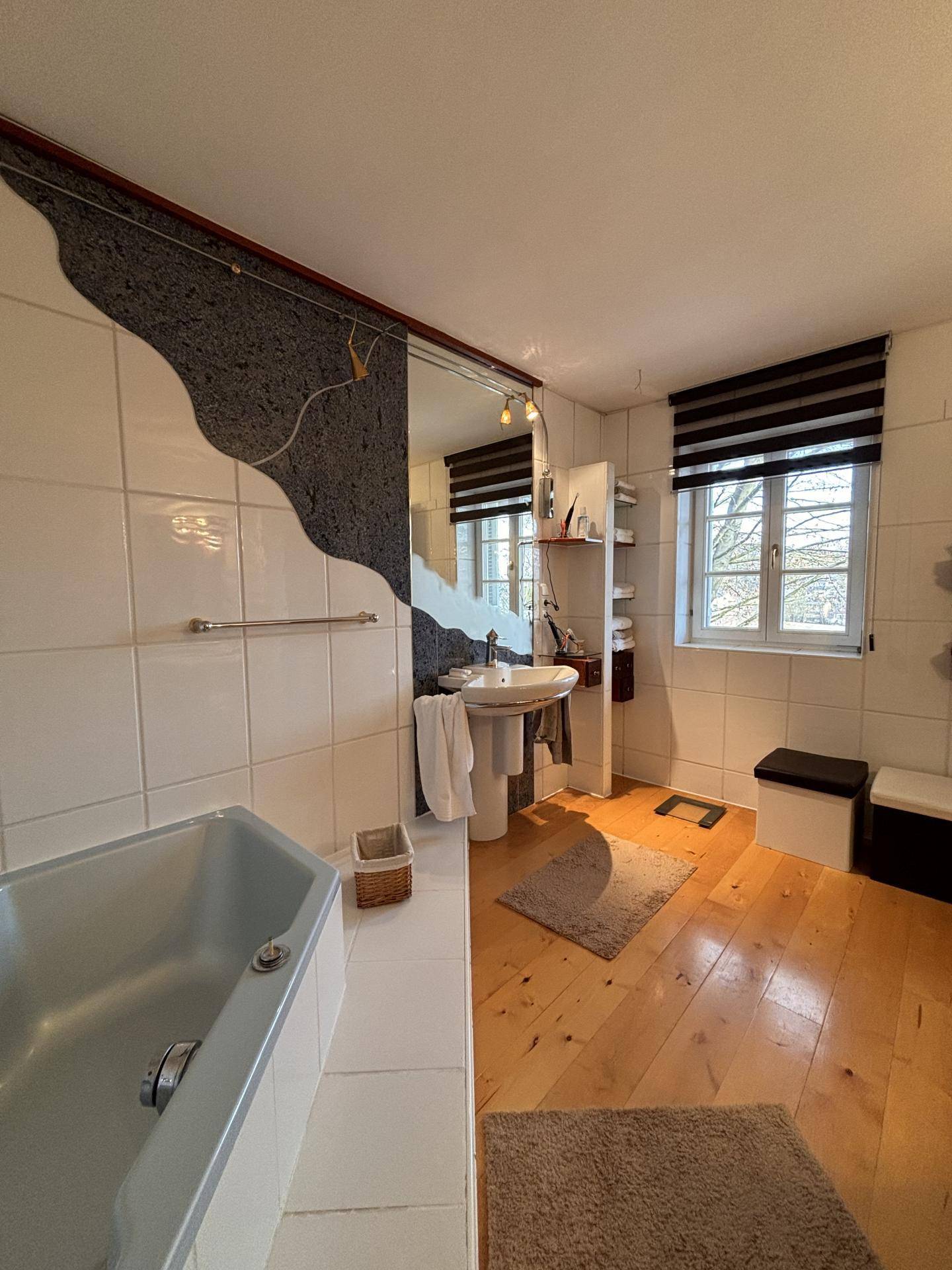 Helles Badezimmer mit Badewanne, Waschtisch und Fenster, das viel Tageslicht spendet.