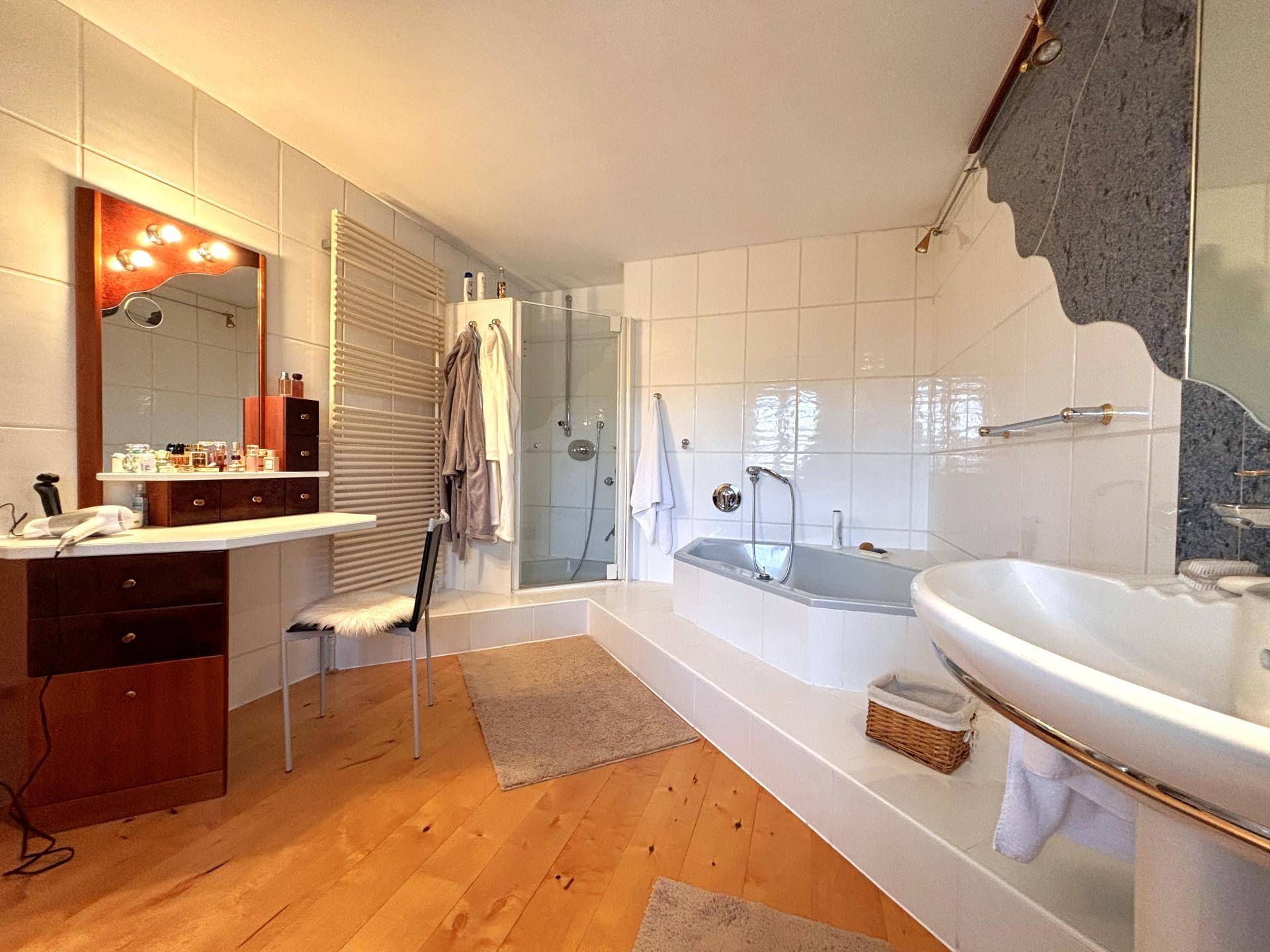 Großes Badezimmer mit Badewanne, Duschkabine, Waschtisch und Holzboden.