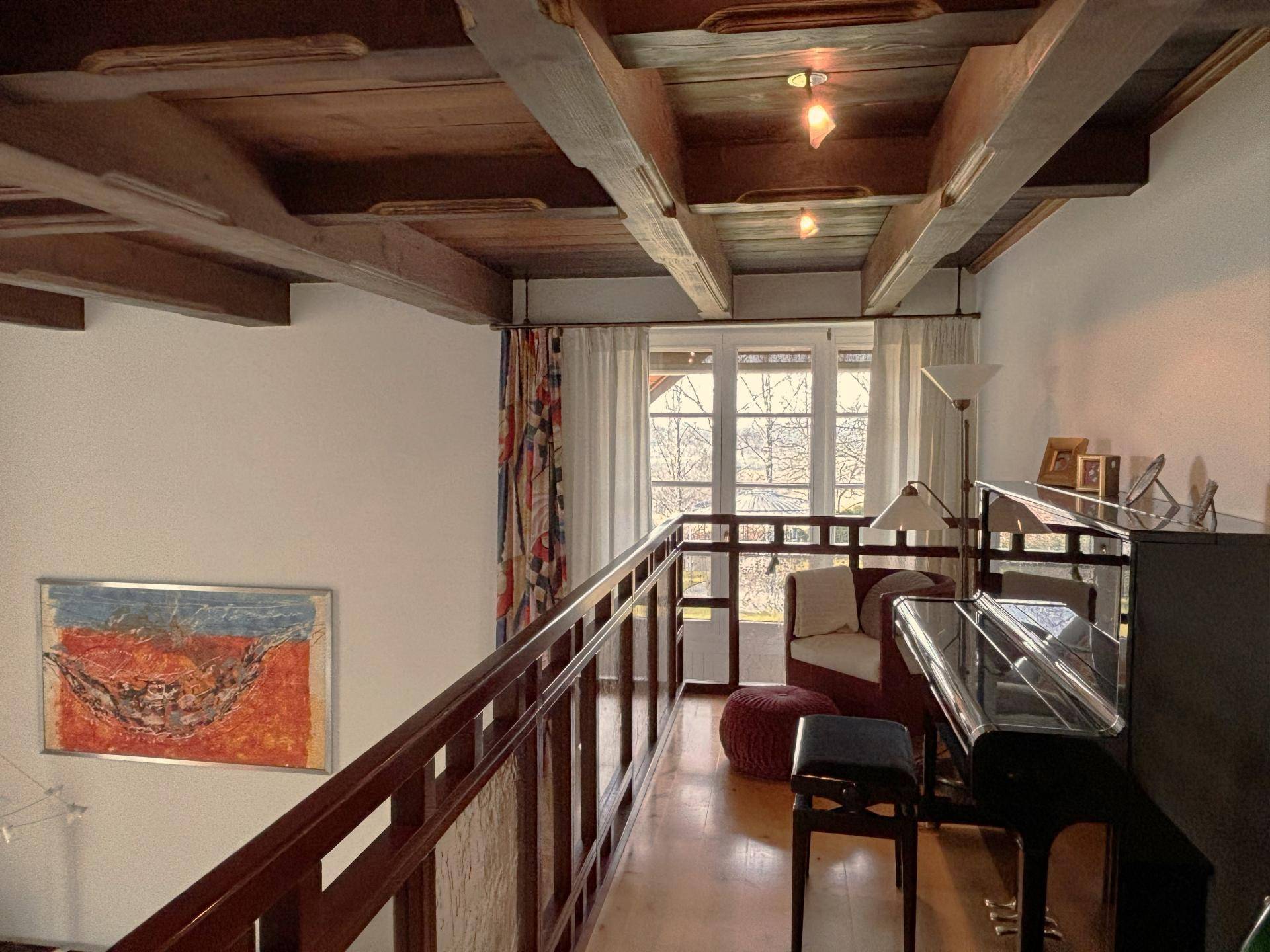 Galeriebereich mit Klavier und Blick auf den unteren Wohnbereich durch ein großes Fenster.