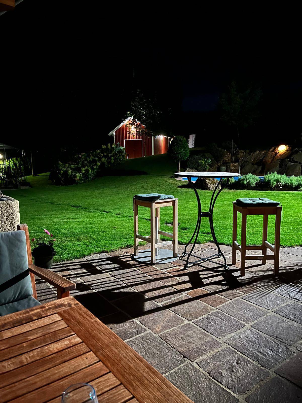 Gemütliche Terrasse am Abend mit Gartenmöbeln und Blick auf den beleuchteten Garten.