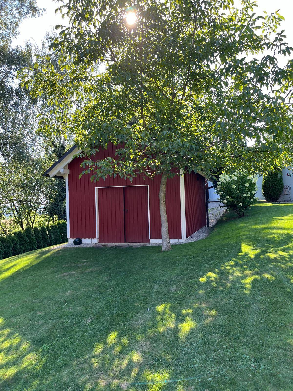 Roter Gartenschuppen in einem gepflegten grünen Garten unter einem großen Baum.
