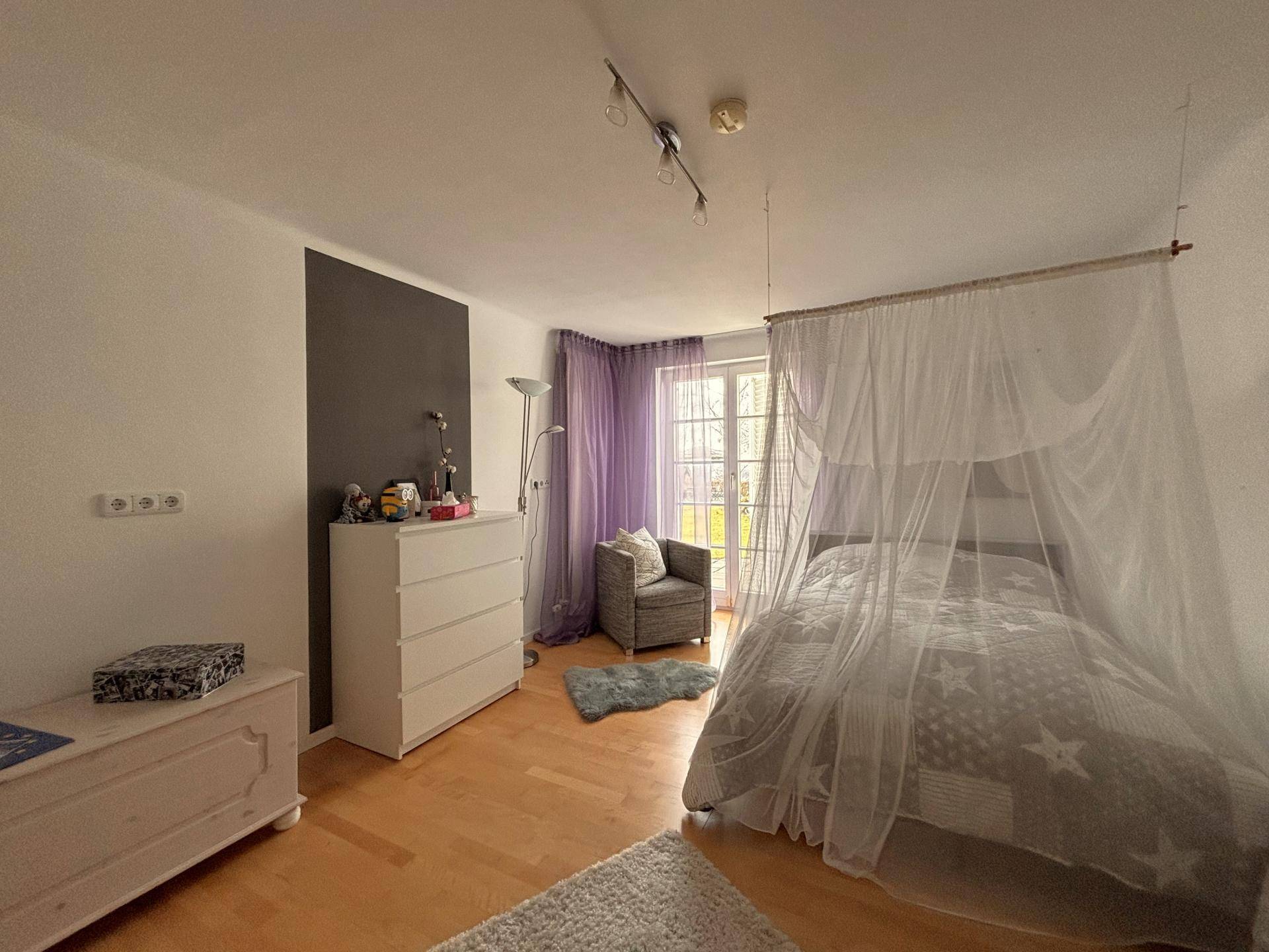 Gemütliches Schlafzimmer mit Holzboden, Kommode und Zugang zu einem Außenbereich durch eine Glastür.