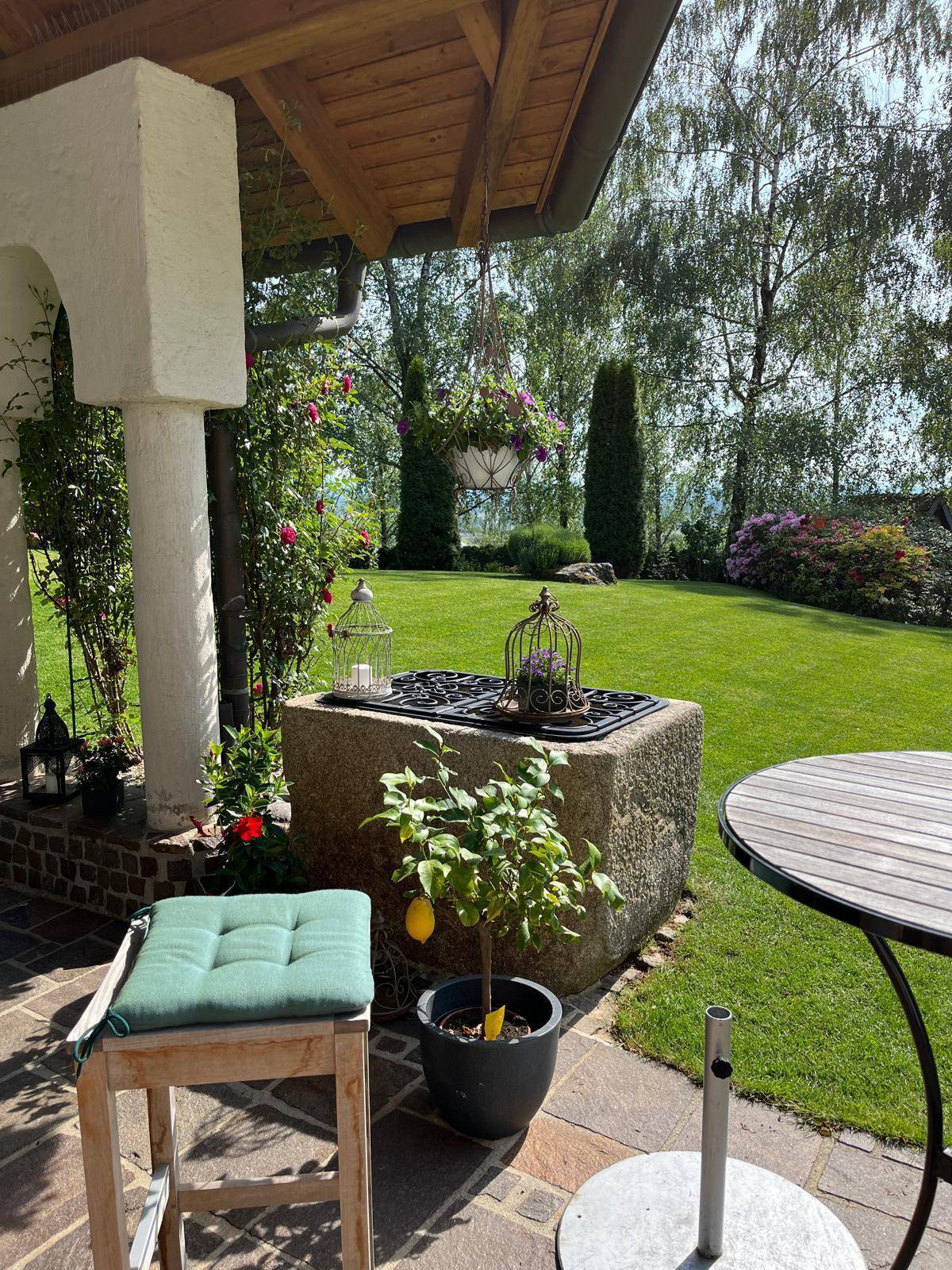 Überdachte Terrasse mit rustikalem Steinbrunnen, Zitronenbaum und weitem Gartenblick.