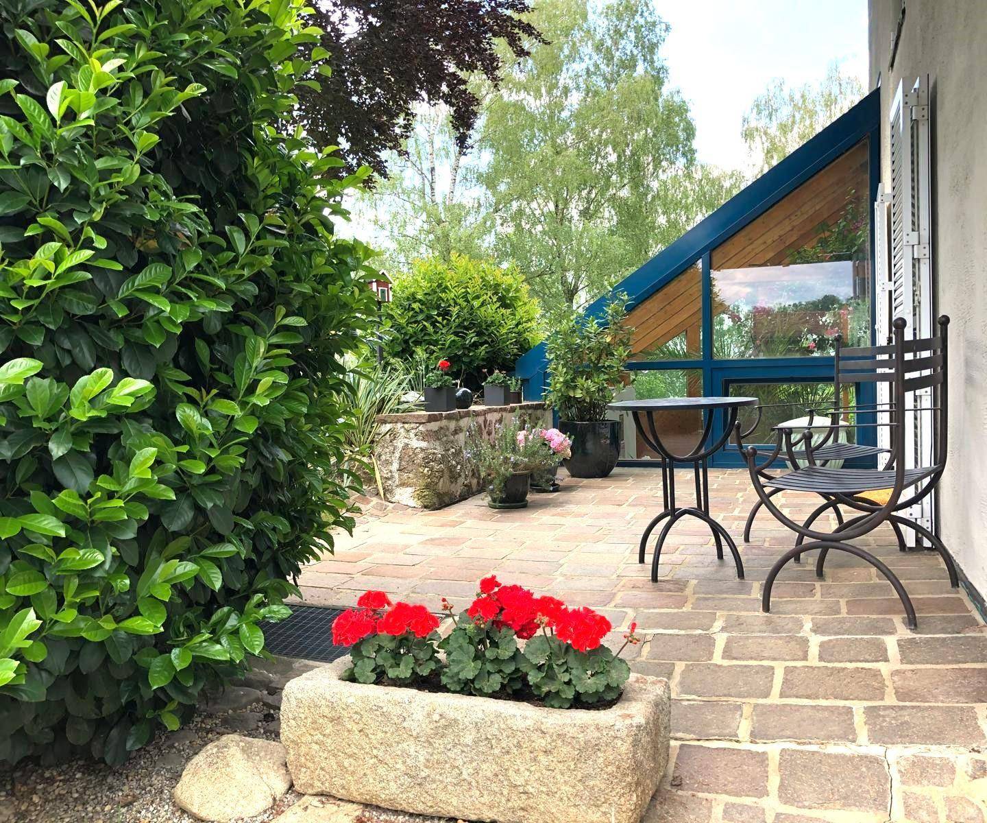 Gemütliche gepflasterte Terrasse mit Gartenmöbeln und Blick auf den verglasten Anbau des Hauses.