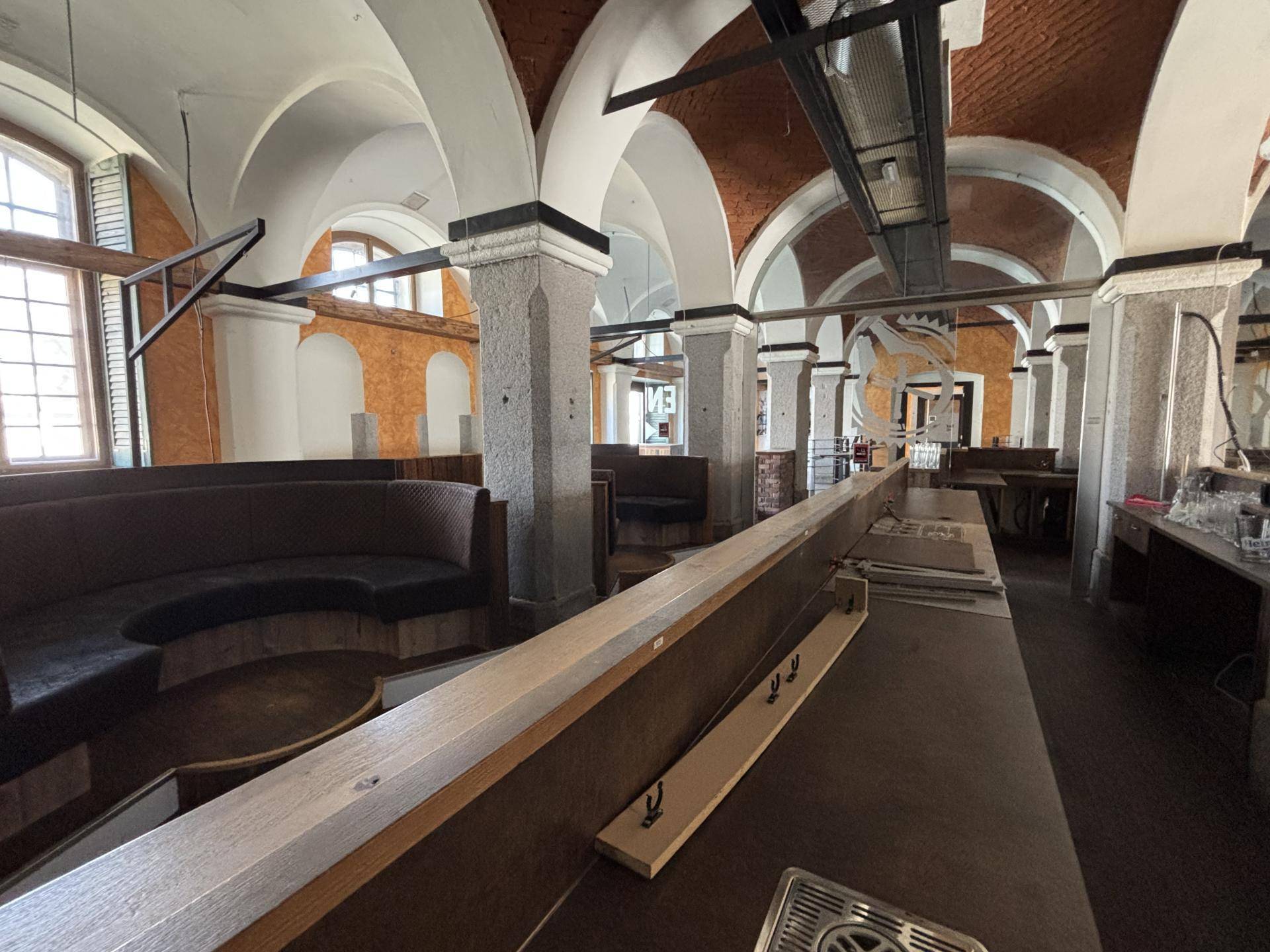 Blick hinter die lange Holztheke auf den Sitzbereich mit runden Bänken und den historischen Gewölbedecken.