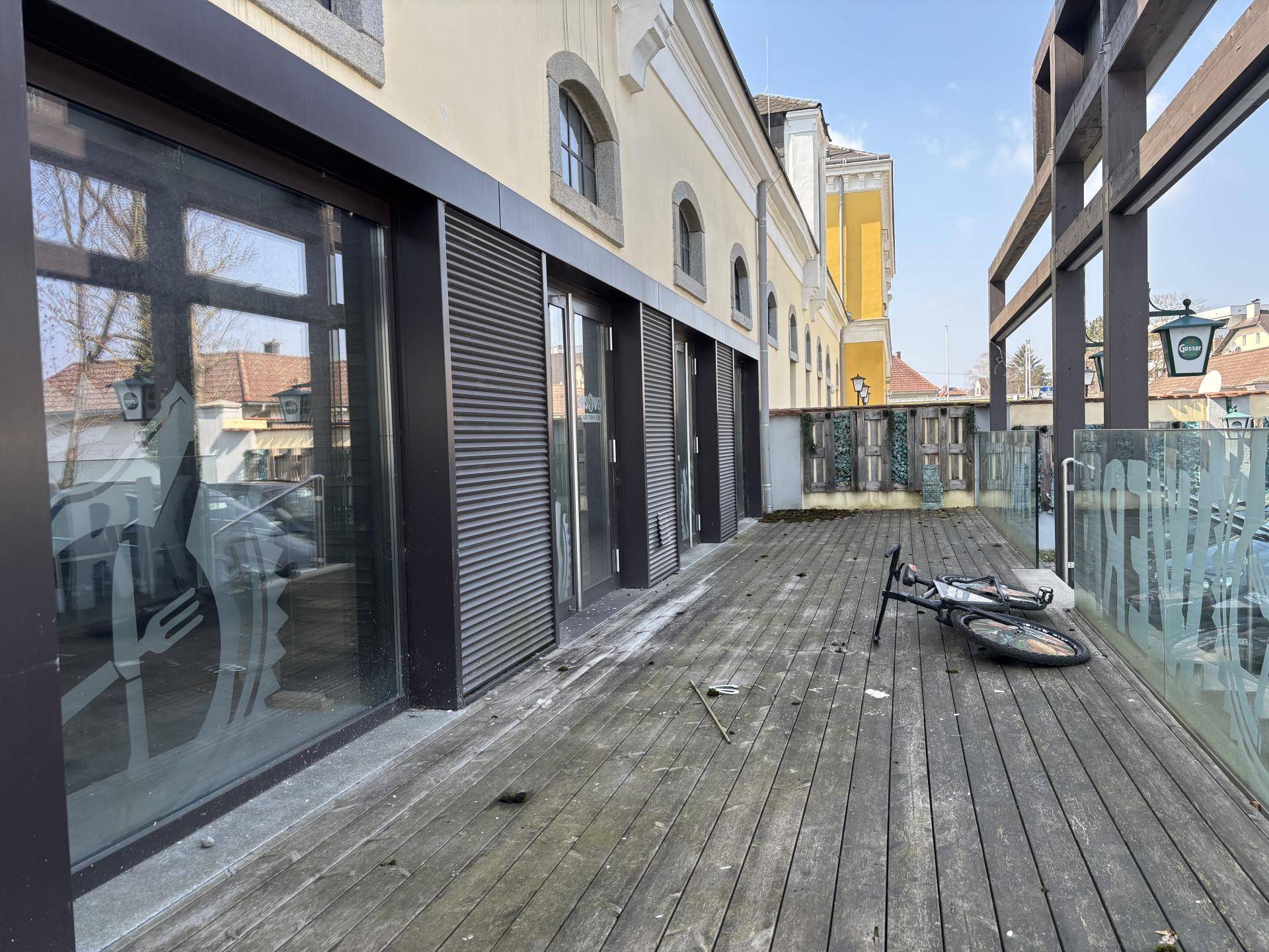 Große Holzterrasse vor dem Gebäude mit großen Glasfronten und Blick auf die Umgebung.