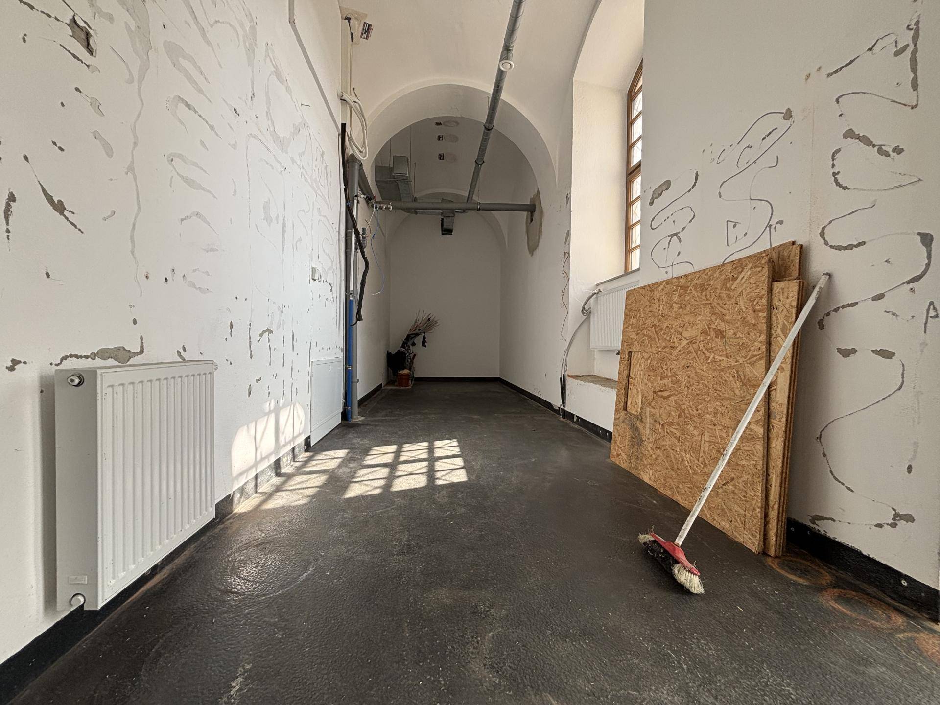 Langer Raum mit gewölbter Decke, weißen Wänden und einem Heizkörper, der als Lager oder Abstellraum dient.