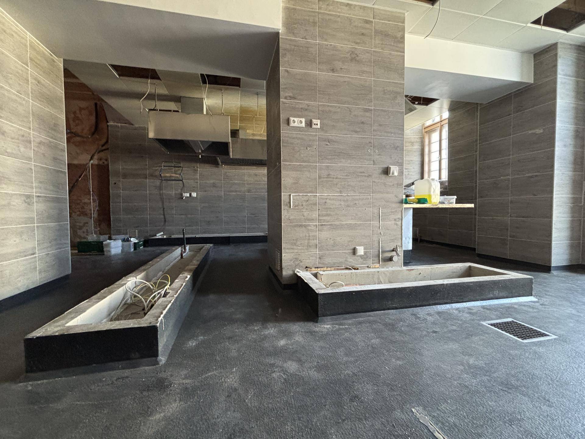 Küche im Umbau mit grauen Fliesenwänden, sichtbaren Installationen und vorbereiteten Arbeitsbereichen.