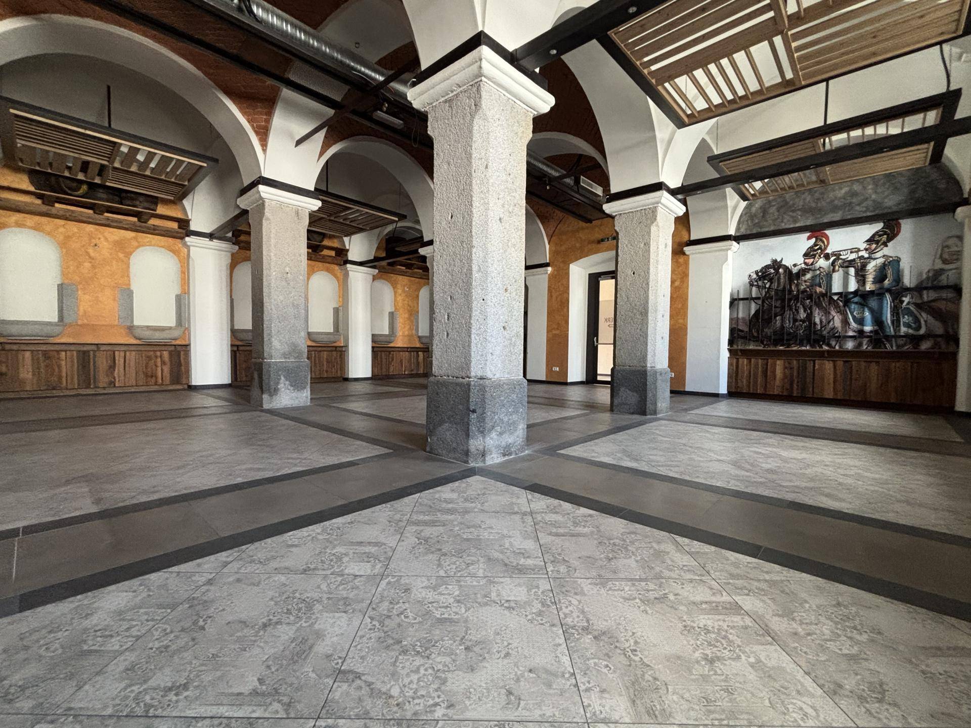 Geräumiger Saal mit beeindruckenden Säulen, Gewölbebögen und einem dekorativen Wandbild im Hintergrund.