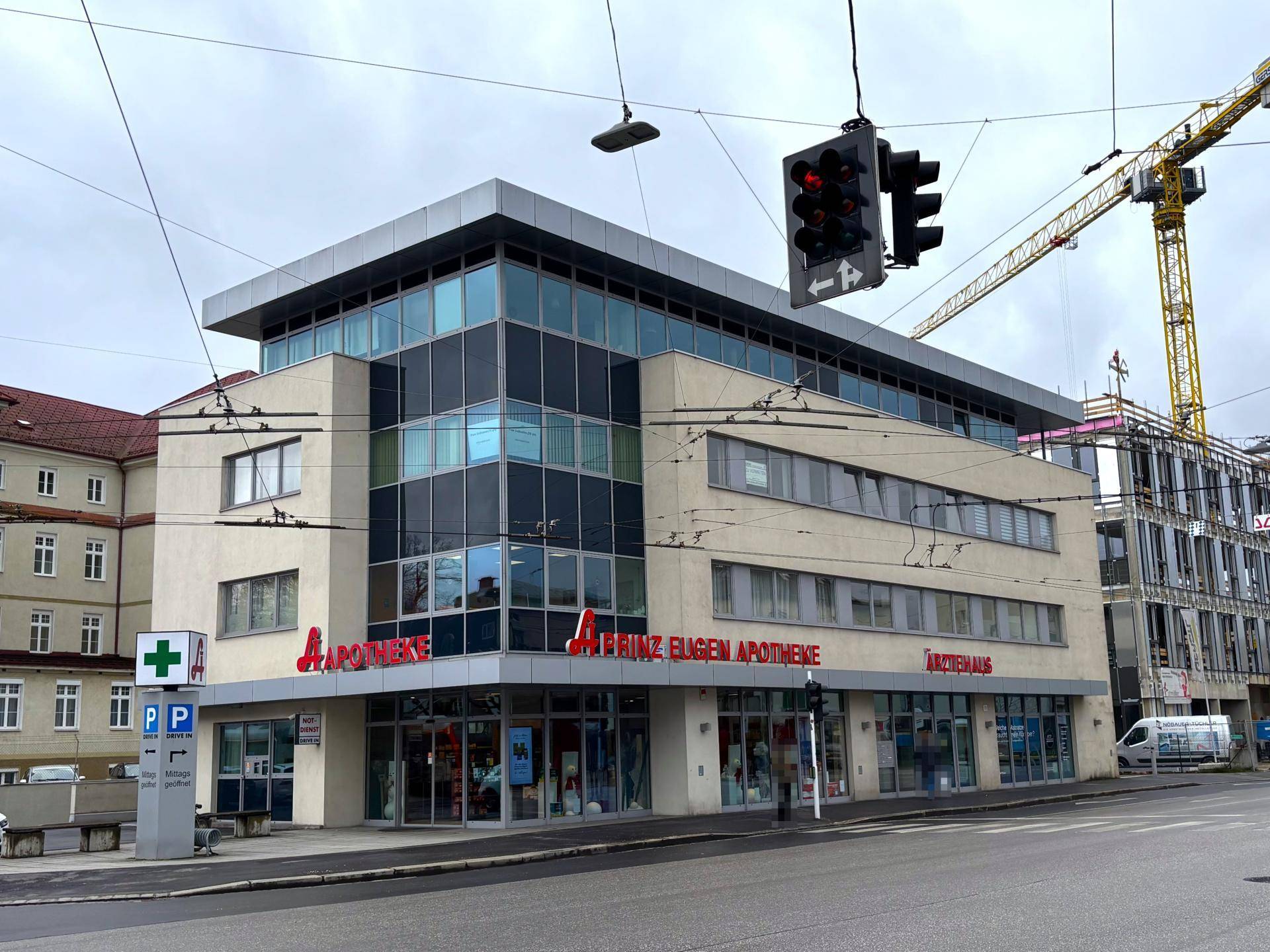 Modernes Geschäftsgebäude mit Apotheke und Ärztehaus im Erdgeschoss, umgeben von städtischer Infrastruktur.