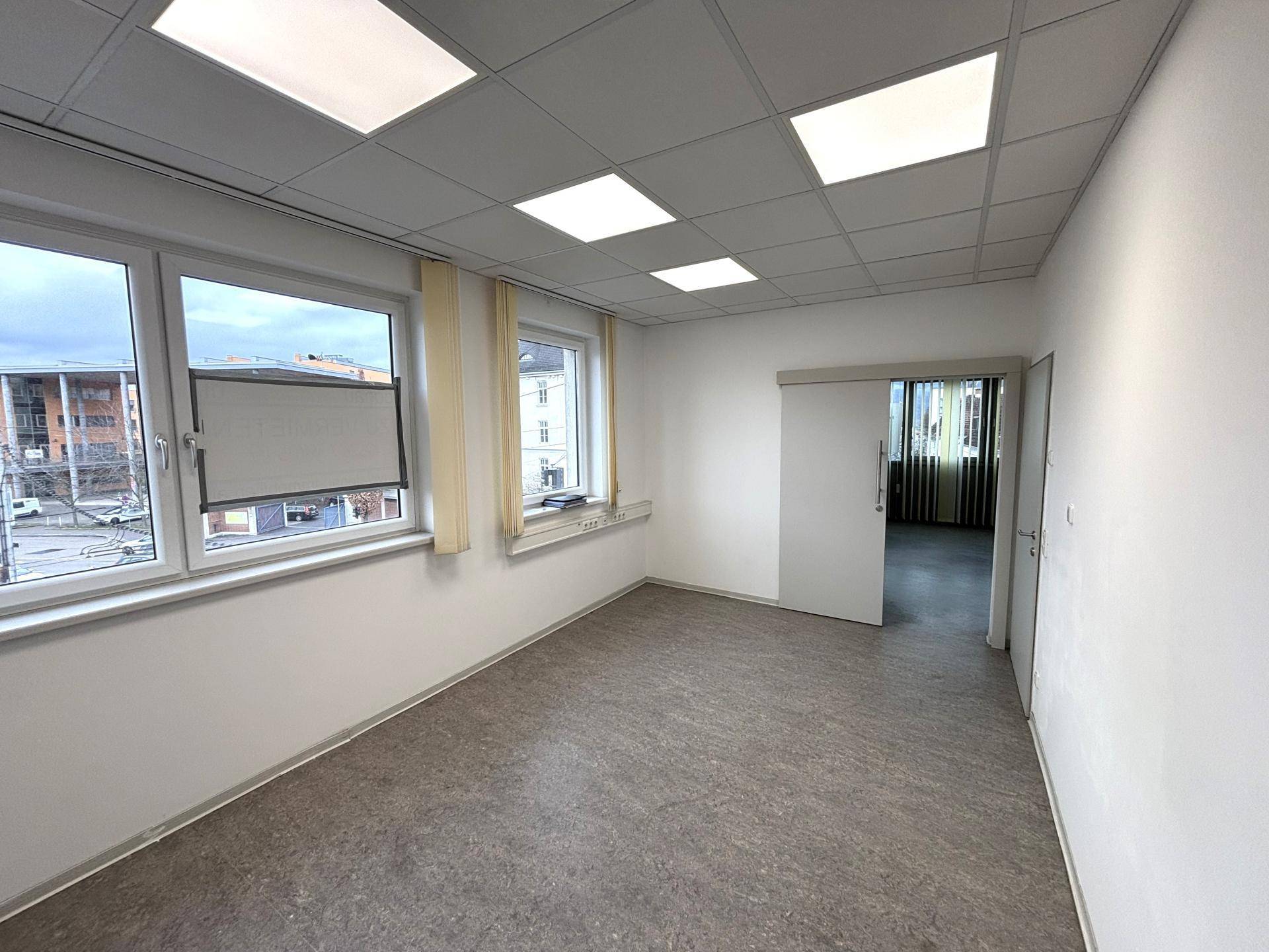 Freundliches Büro mit mehreren Fenstern, die Tageslicht hereinlassen, und einem praktischen Linoleumboden.