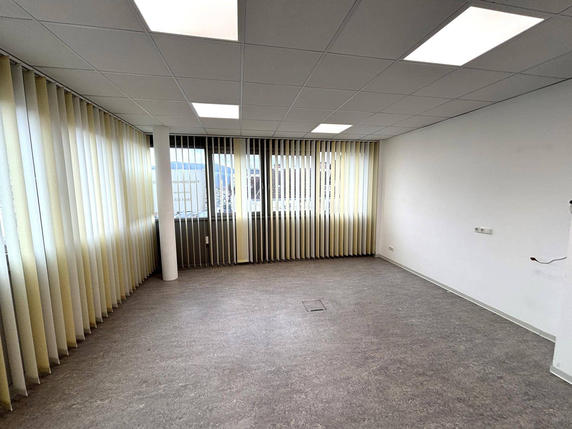 Helles Büro mit großen Fenstern, vertikalen Jalousien und einem strapazierfähigen Linoleumboden.