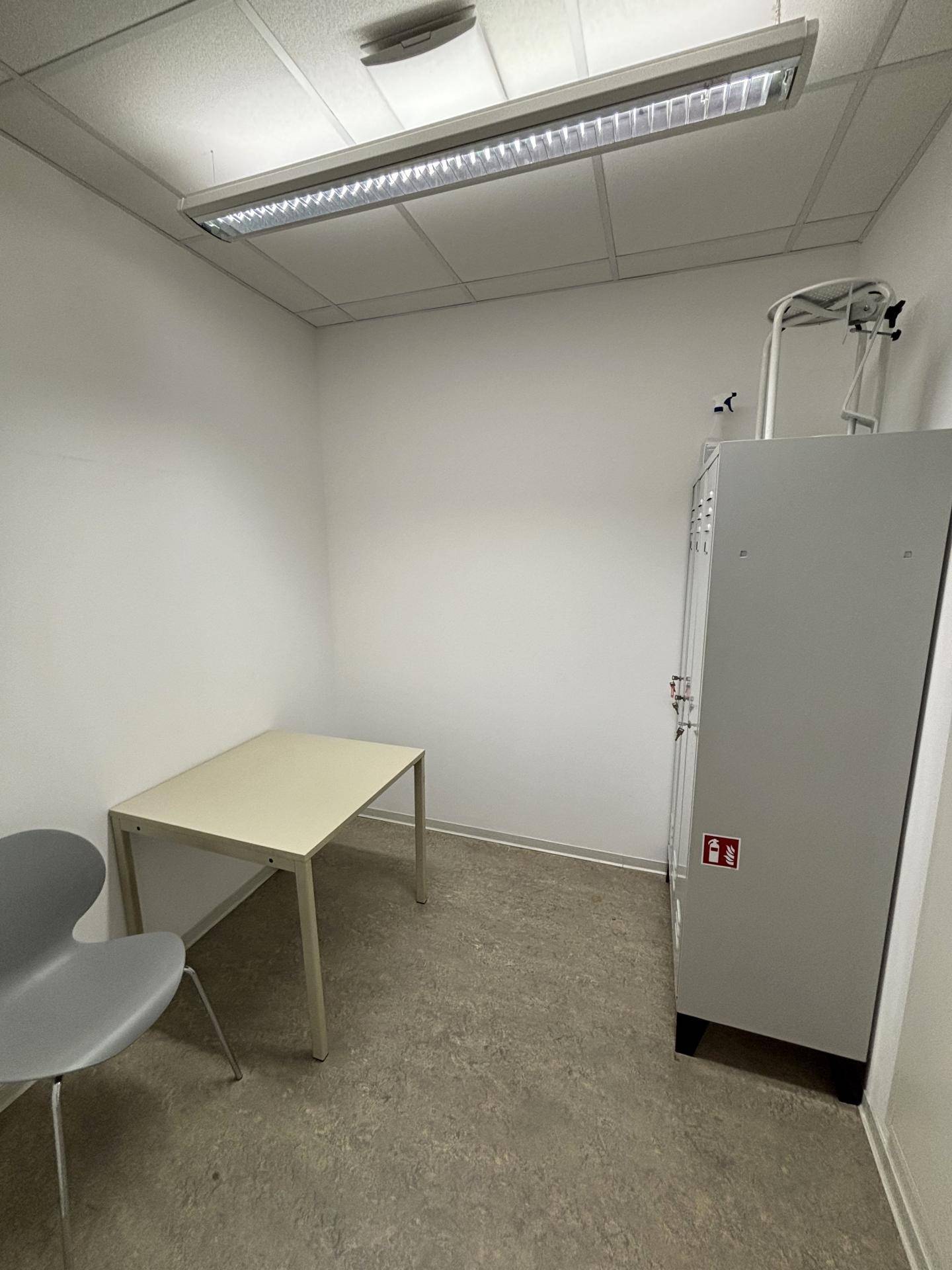 Kleiner, funktionaler Raum mit Tisch, Stuhl und Spind, ideal für Besprechungen oder Umkleide.