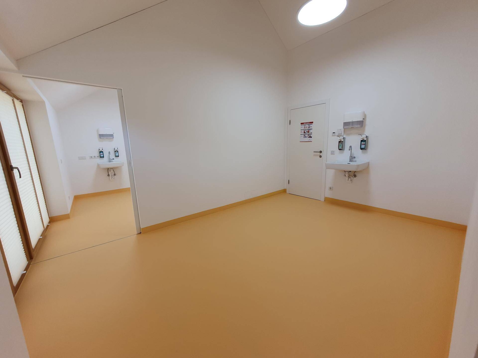 Heller Innenraum mit orangefarbenem Boden, weißen Wänden und Waschbecken, ideal für medizinische Nutzung.