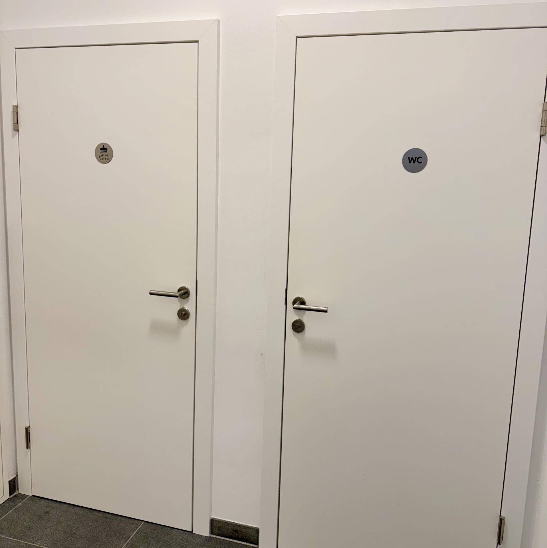 Zwei weiße Türen in einem Flur, eine führt zur Toilette und die andere zu einer Dusche.