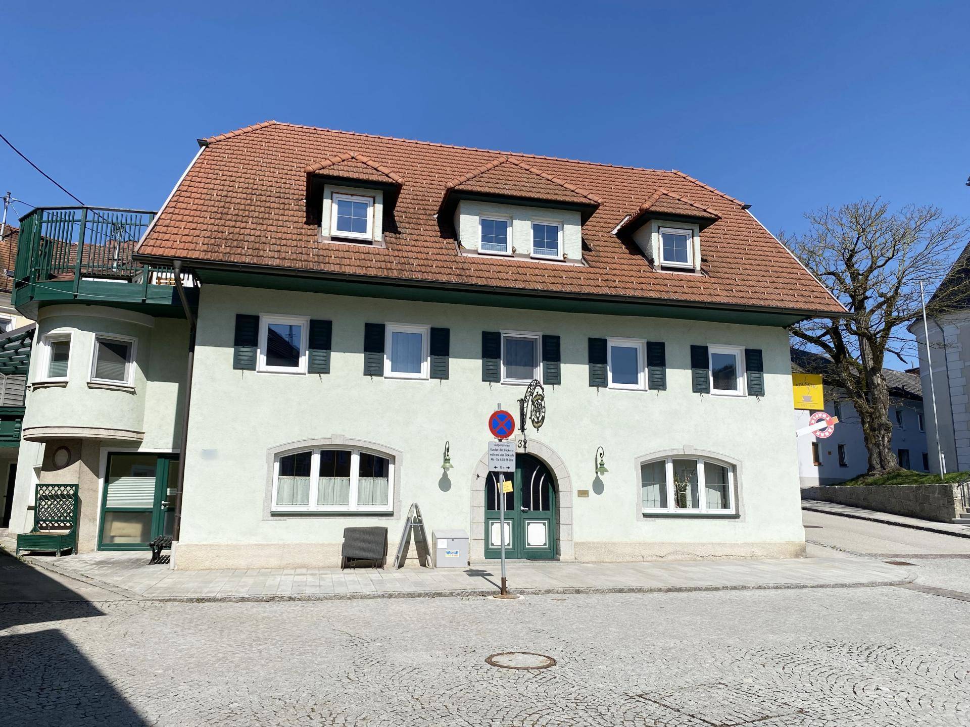 Gesamtansicht des Gebäudes mit traditionellem Satteldach, grünen Fensterläden und gepflastertem Vorplatz.