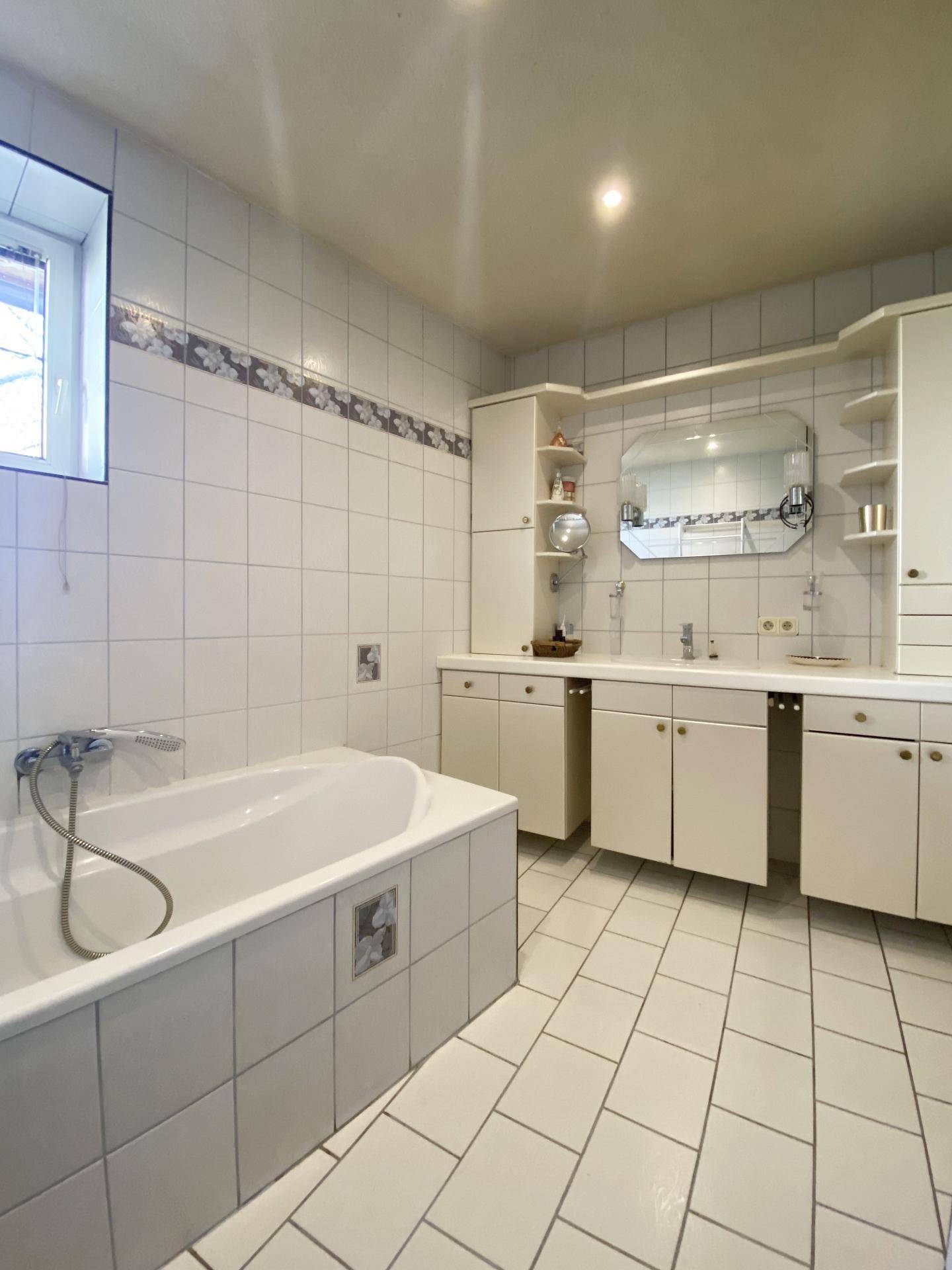 Helles Badezimmer mit Badewanne, Doppelwaschbecken und weißen Fliesen im 80er-Jahre-Stil.