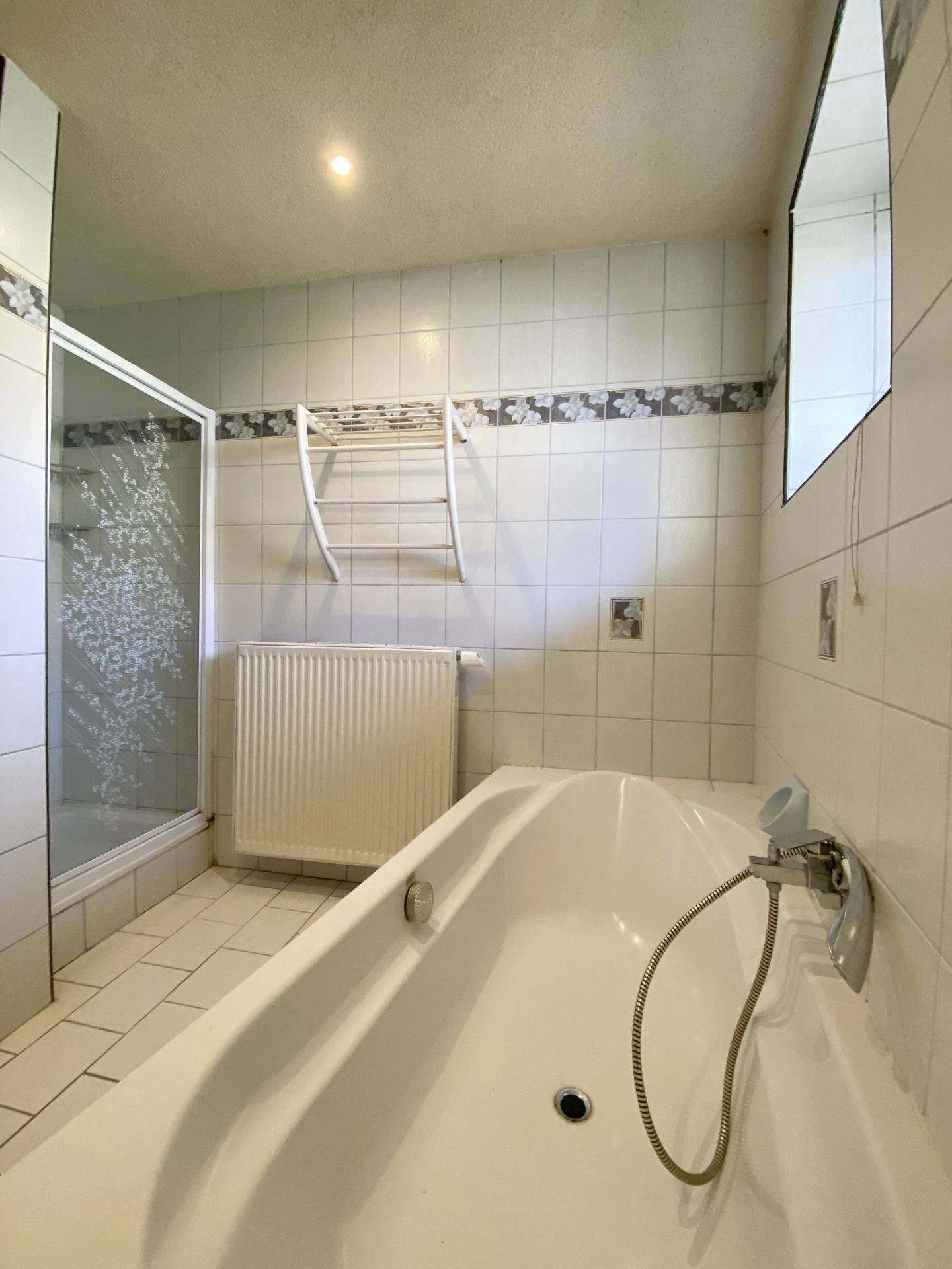 Badezimmer mit Badewanne, Duschkabine und weißen Fliesen, die ein klassisches Muster aufweisen.