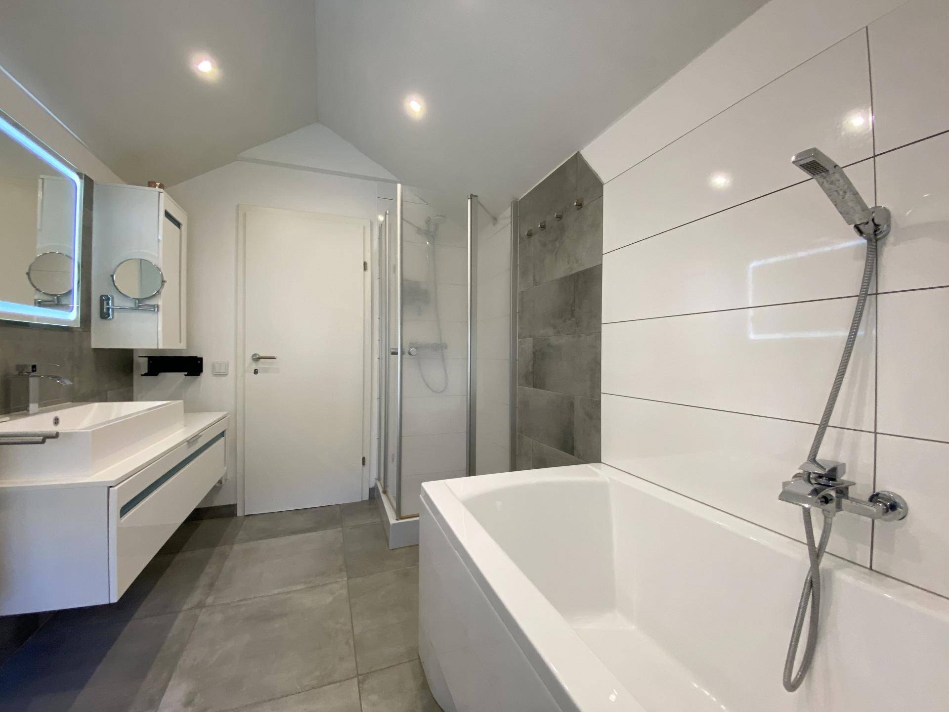 Modernes Badezimmer mit Badewanne, Duschkabine und Waschtisch, ausgestattet mit grauen und weißen Fliesen.