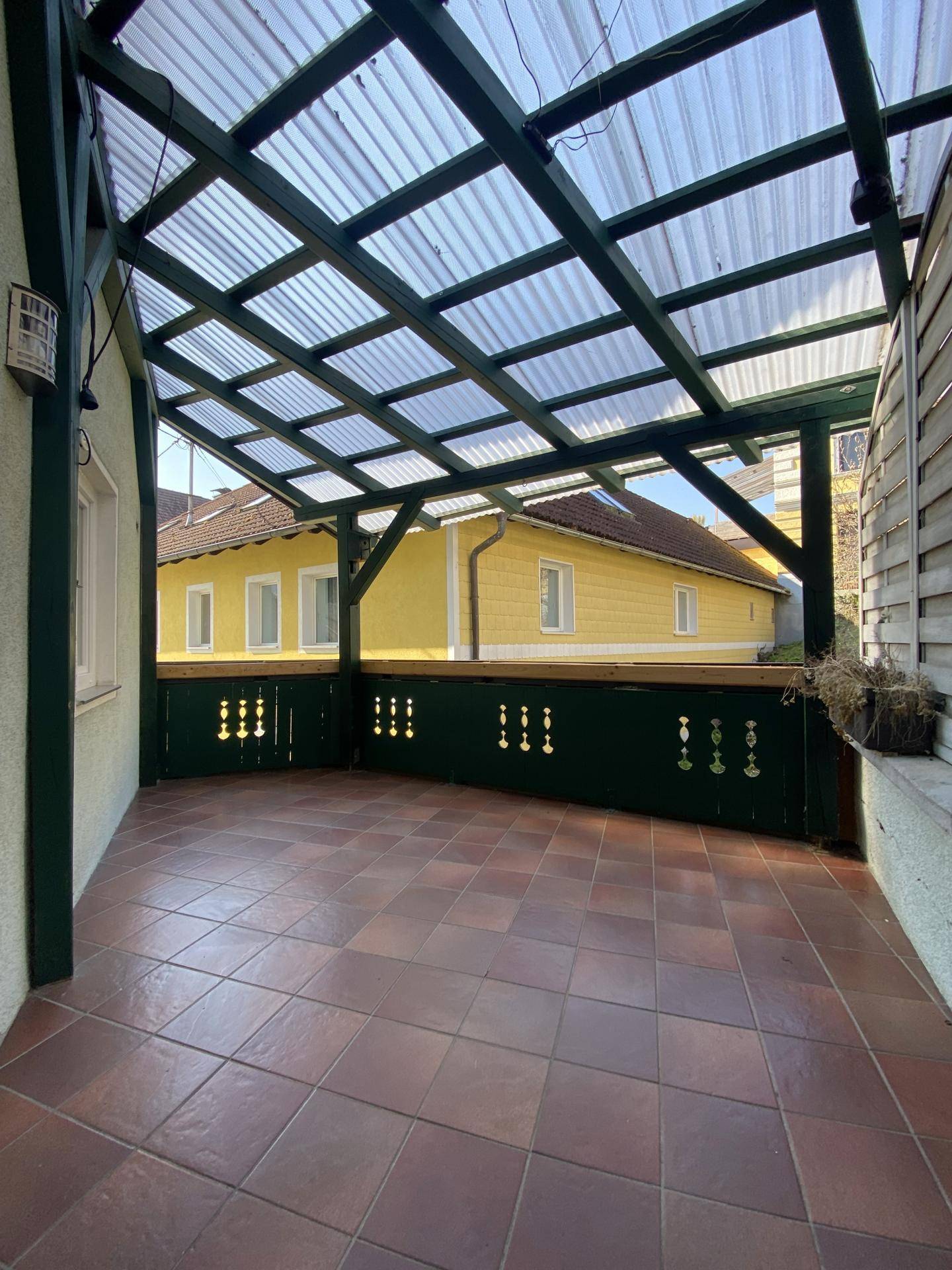 Überdachte Terrasse mit Terrakotta-Fliesen und Blick auf die umliegenden Gebäude.