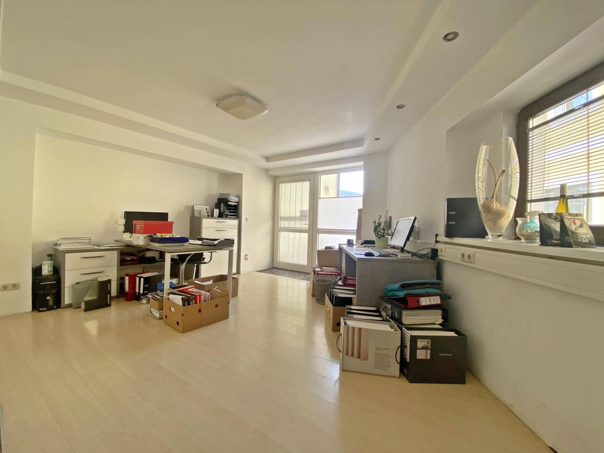 Helles Büro mit hellem Holzboden, großen Fenstern und Zugang zu einem Balkon oder einer Terrasse.