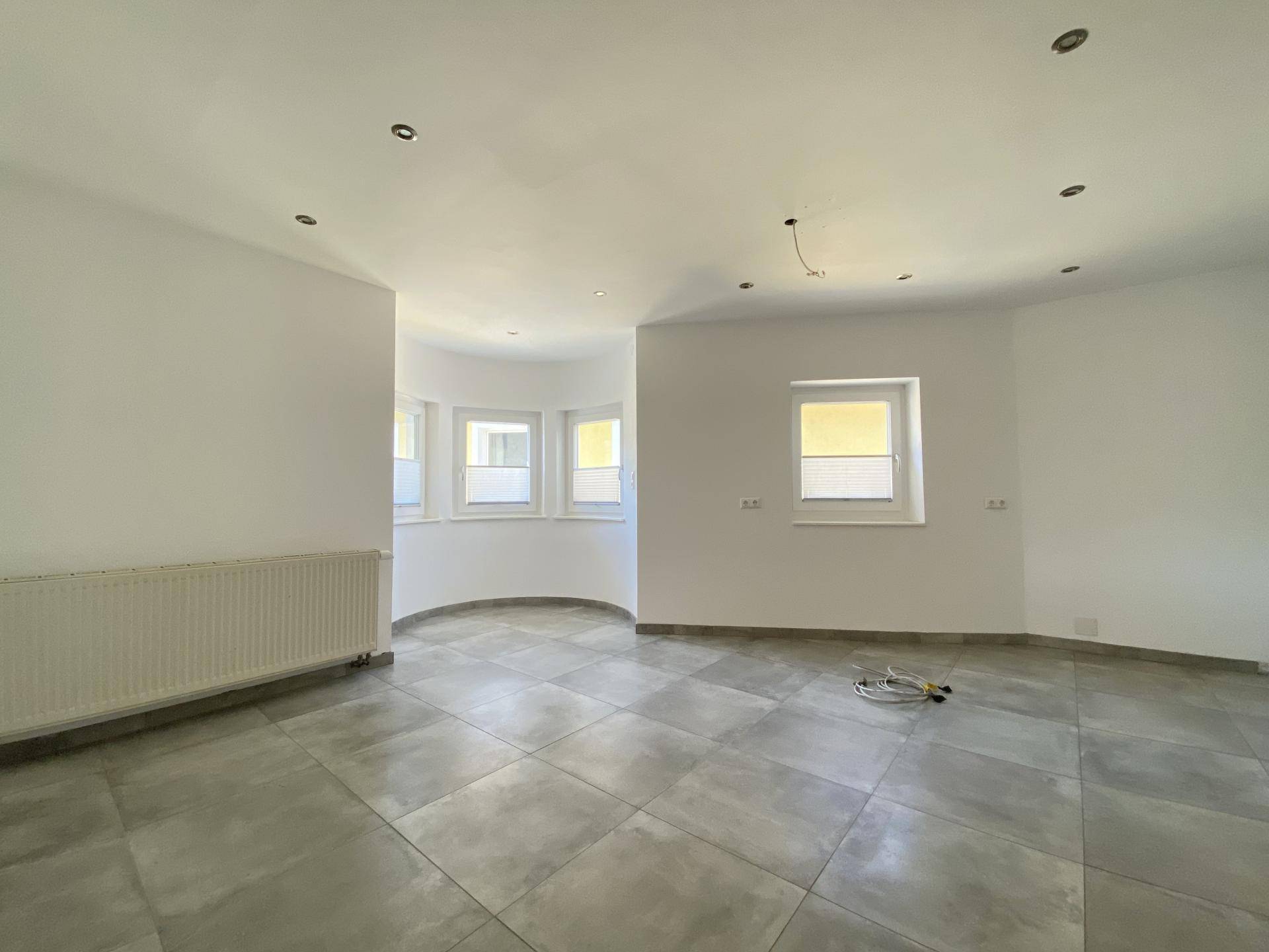 Geräumiger, heller Raum mit grauen Fliesen und einer Fensterfront, die viel Tageslicht hereinlässt.