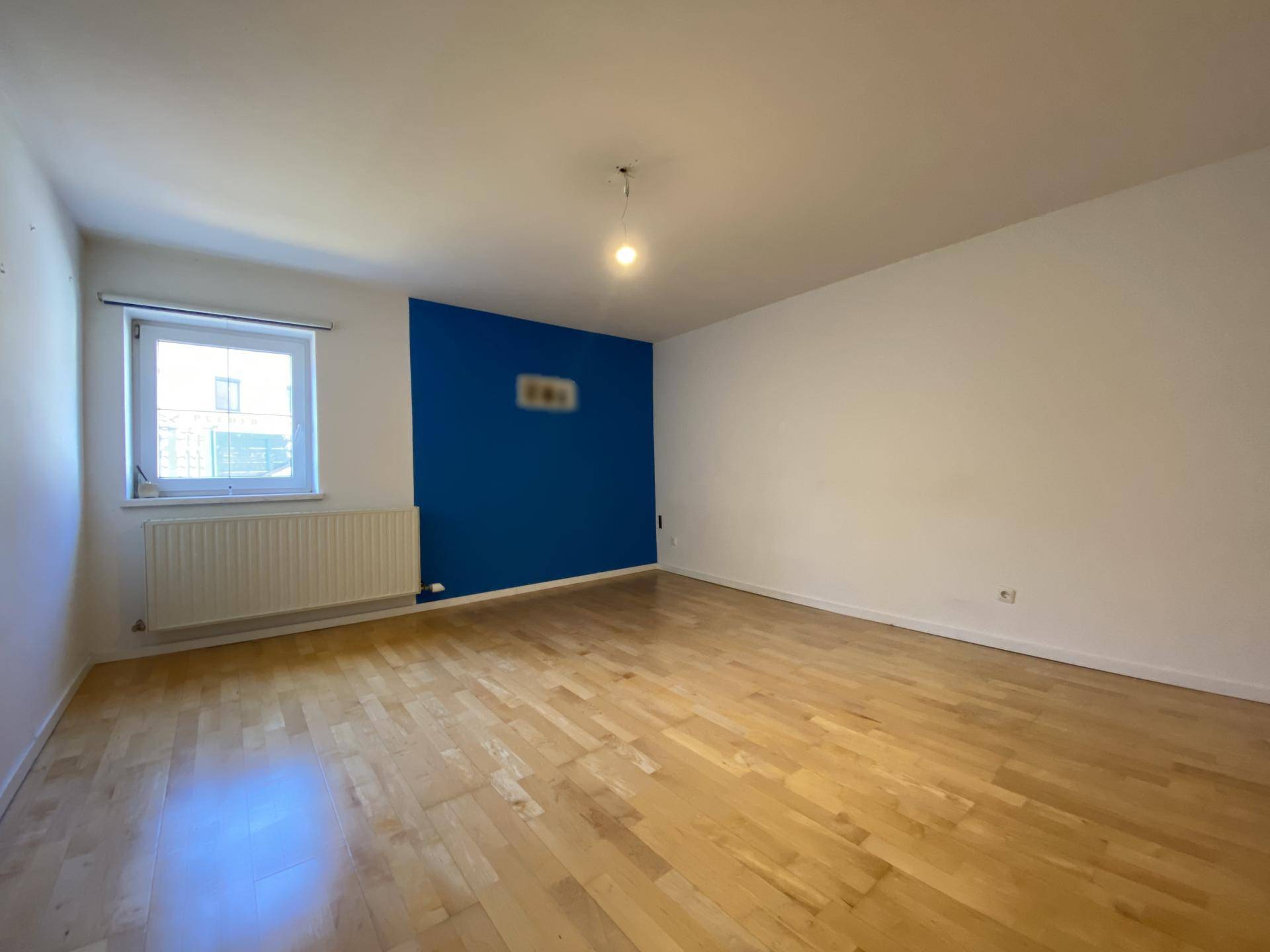 Helles Zimmer mit Holzboden und einer blauen Akzentwand, die einen modernen Kontrast schafft.