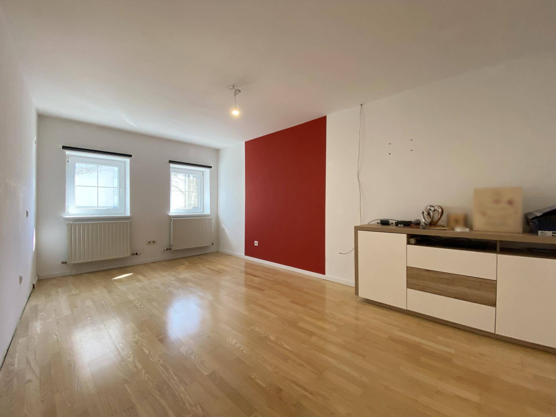 Geräumiges Zimmer mit Holzboden und einer roten Akzentwand, die einen lebendigen Farbtupfer setzt.
